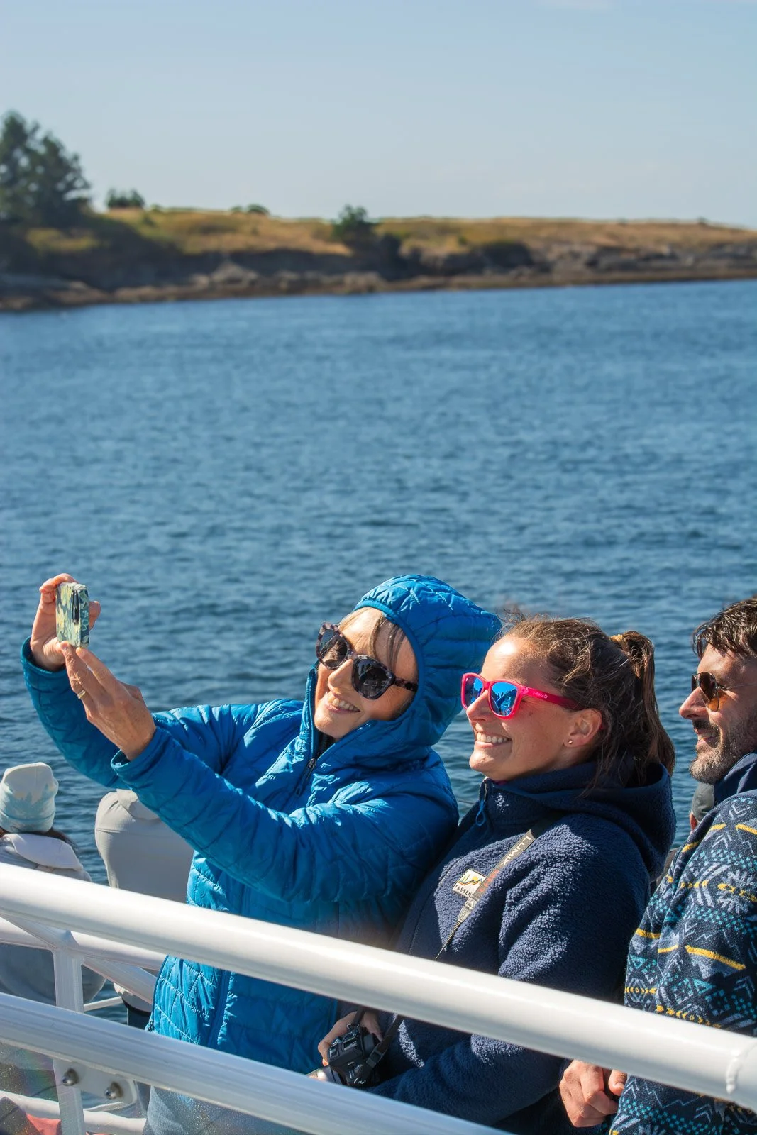 Three friends taking a selfie on a boat with water and a distant shoreline in the background