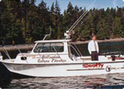 A man standing on a white boat named 'Sea Scout' docked near a forested shoreline.