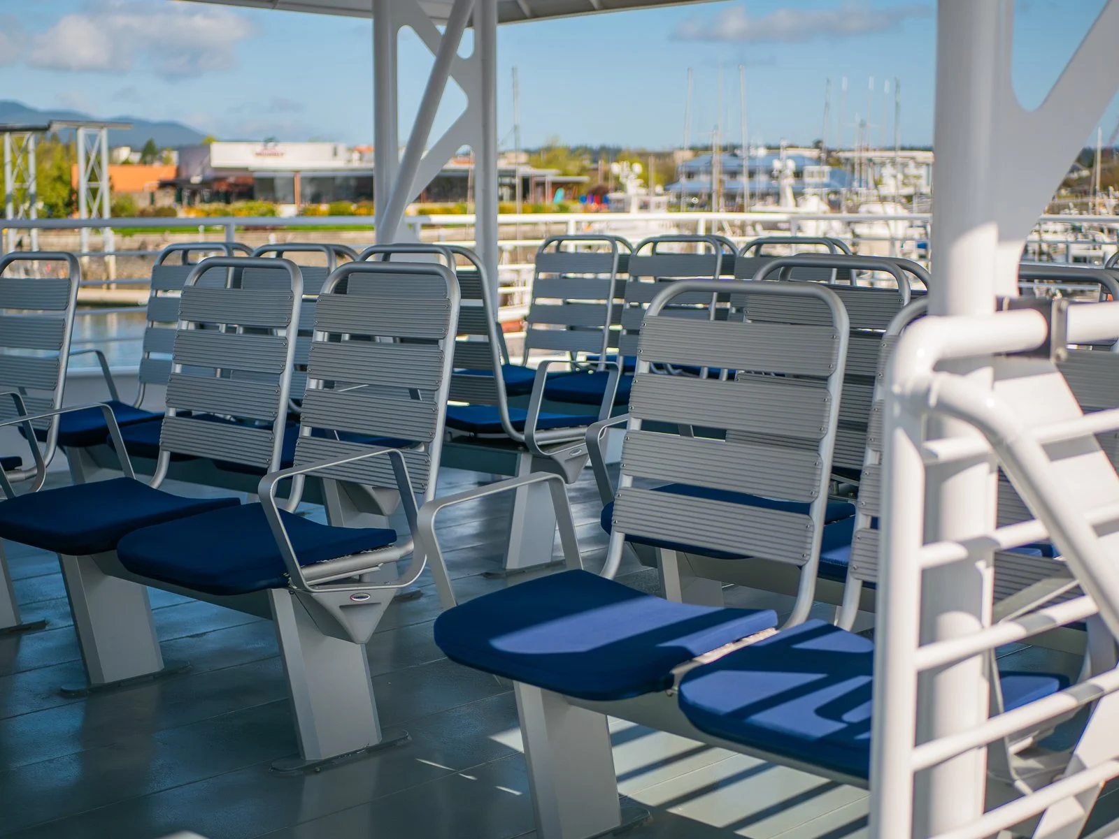 Multiple blue cushioned chairs with metal frames on a boat deck, overlooking marina with boats and buildings in the background.