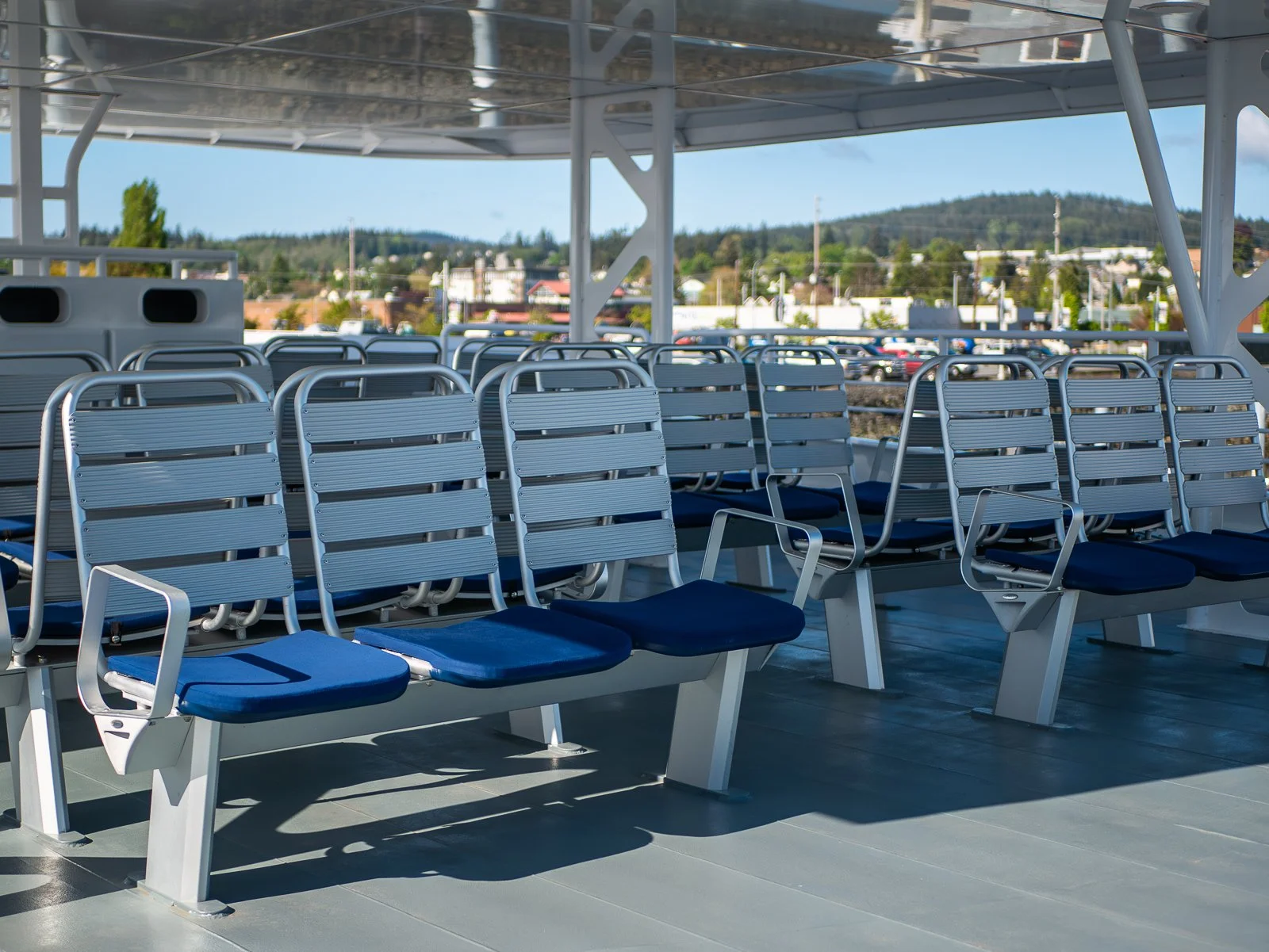 Empty outdoor passenger ferry deck with chairs and a view of a town and hills in the background.