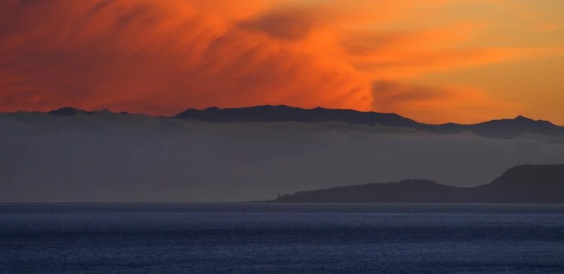 Sunset over mountains with a body of water in the foreground.