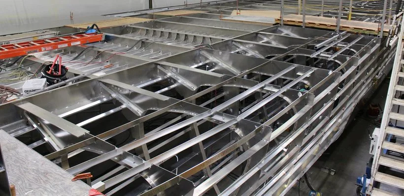 Steel framework of a building under construction, with metal beams and structural supports visible, along with some construction tools and equipment.