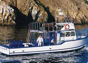 A small boat with a cabin and open deck, sailing on water near rocky cliffs.