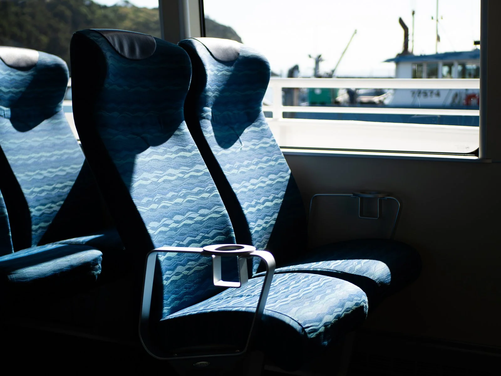 Empty blue patterned seats inside a train with a window showing boats and water outside.