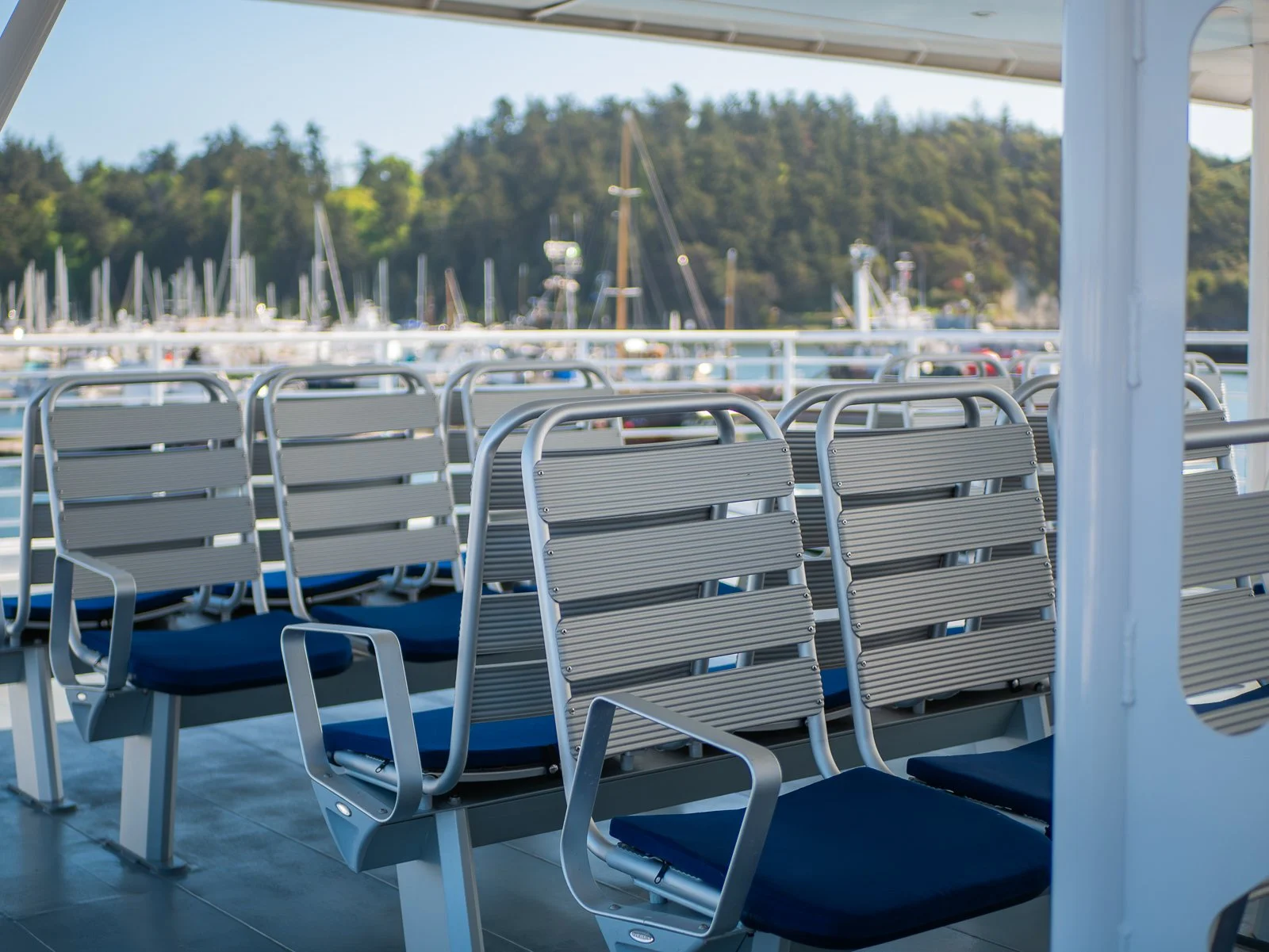 Empty seats on a boat deck overlooking a marina with boats and green hills in the background.