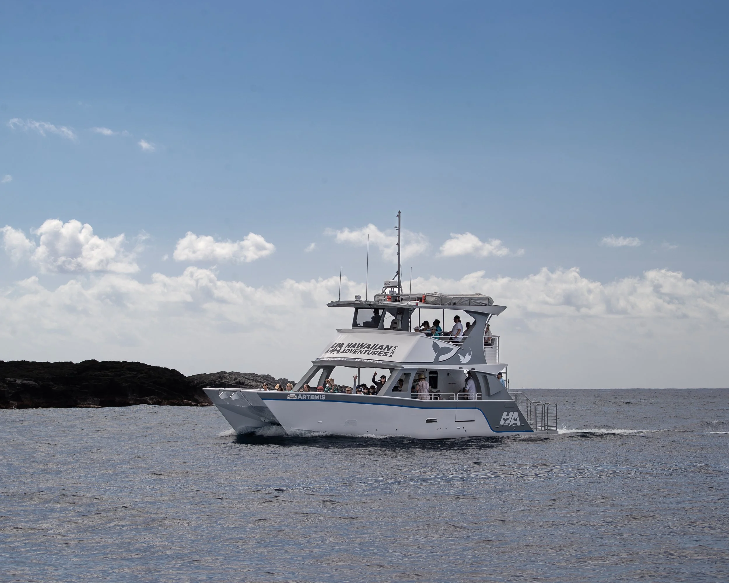 A white boat with people on the deck sailing in the water under a blue sky with scattered clouds.