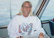 Woman with long blonde hair wearing a white hoodie, holding a fish on a boat