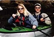 A woman and a man sitting in a green kayak on a water body, smiling at the camera.