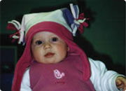 Baby wearing a pink and white hat and a pink outfit, sitting in a car seat.