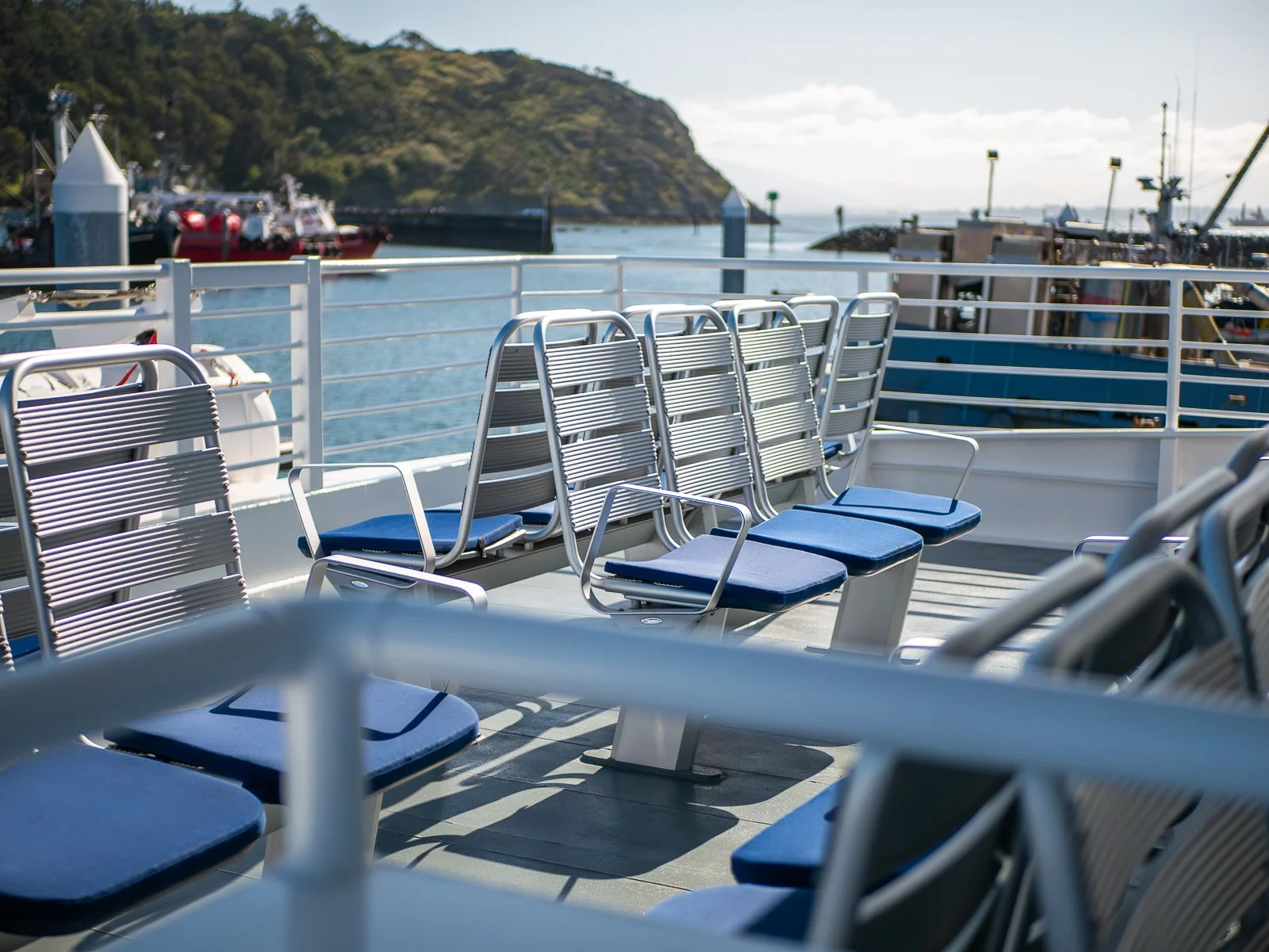 Seats on a ferry deck with a harbor and boats in the background under a sunny sky.