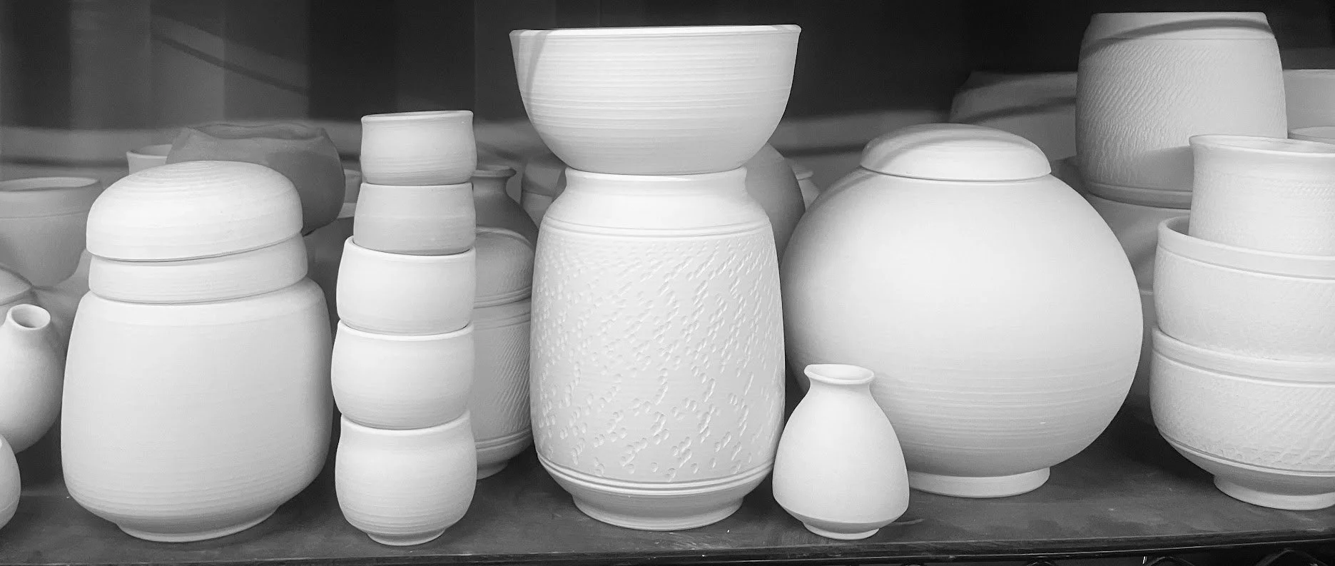 Collection of unfinished and glazed pottery vases and bowls on display.