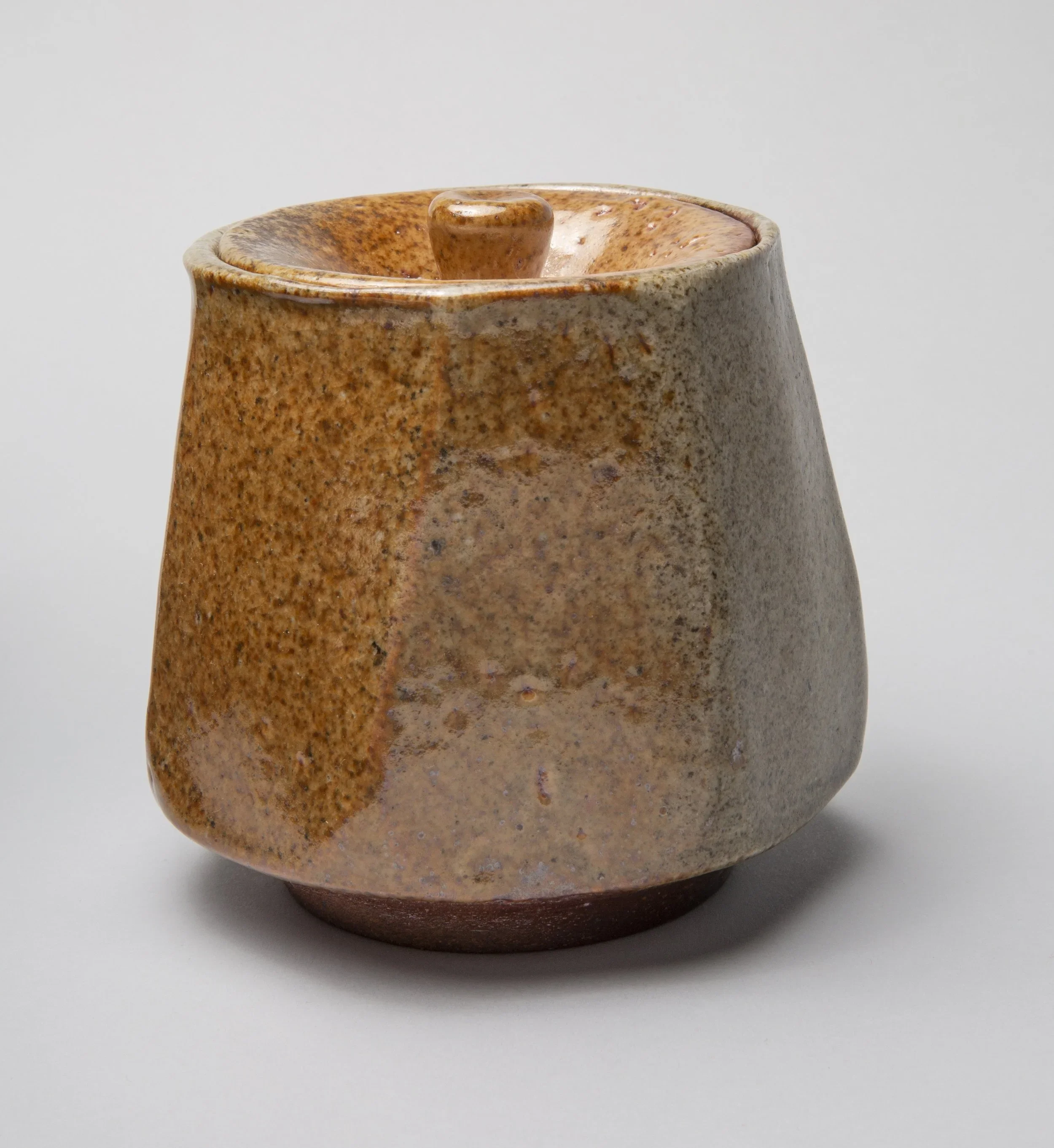A handmade ceramic mortar and pestle in earthy tones, with a speckled glaze finish, positioned against a plain white background.