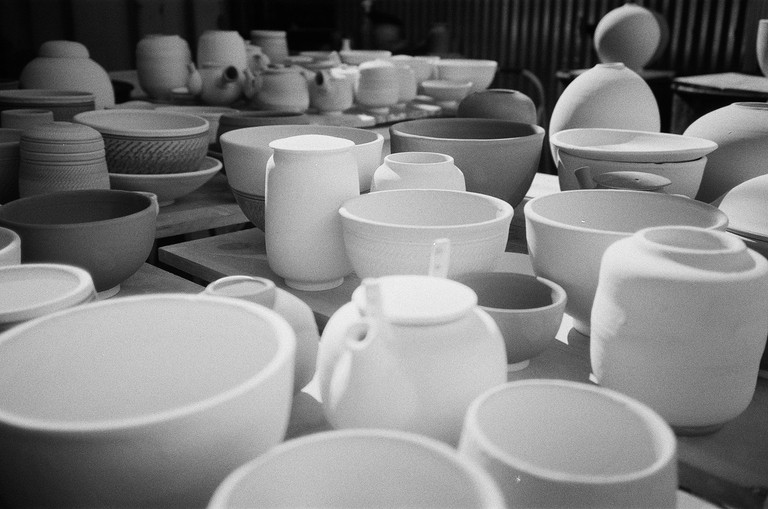 Collection of plain ceramic bowls and cups on tables outdoors.