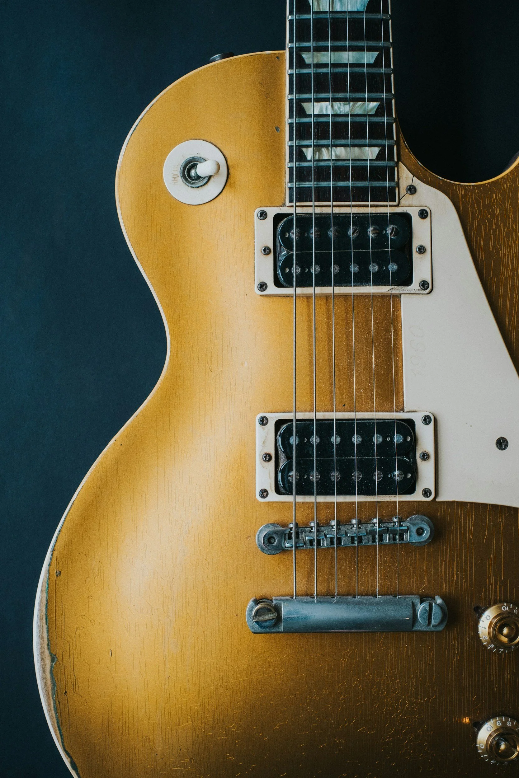 Close-up of a vintage electric guitar showing the strings, pickups, bridge, and part of the body which has a worn, distressed finish.