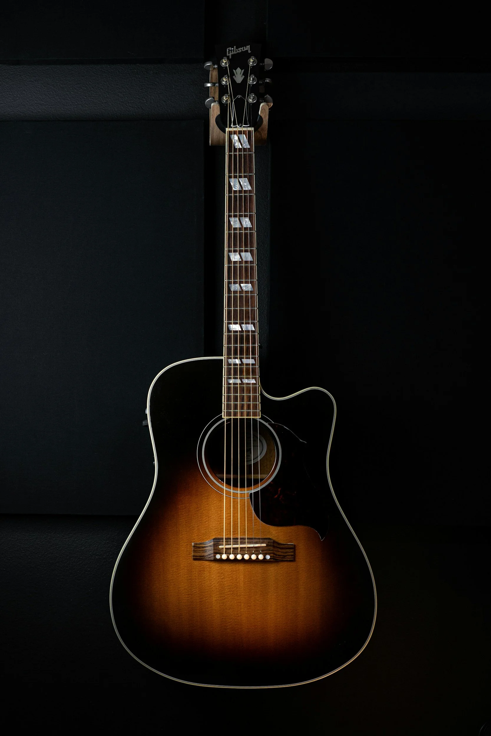 A Gibson acoustic guitar with a sunburst finish, standing against a dark background.