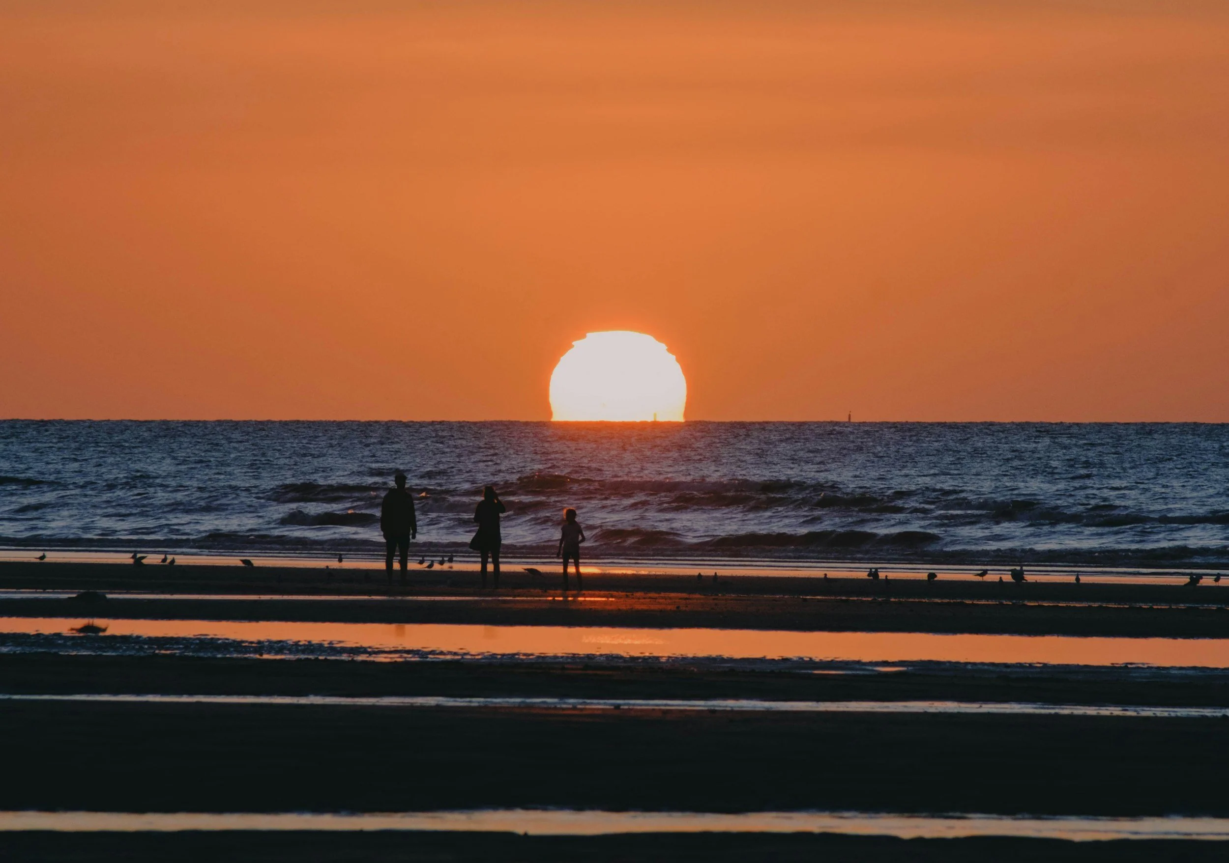 Coucher de soleil sur la mer avec trois personnes qui regardent l'horizon, ambiance orange et sombre.