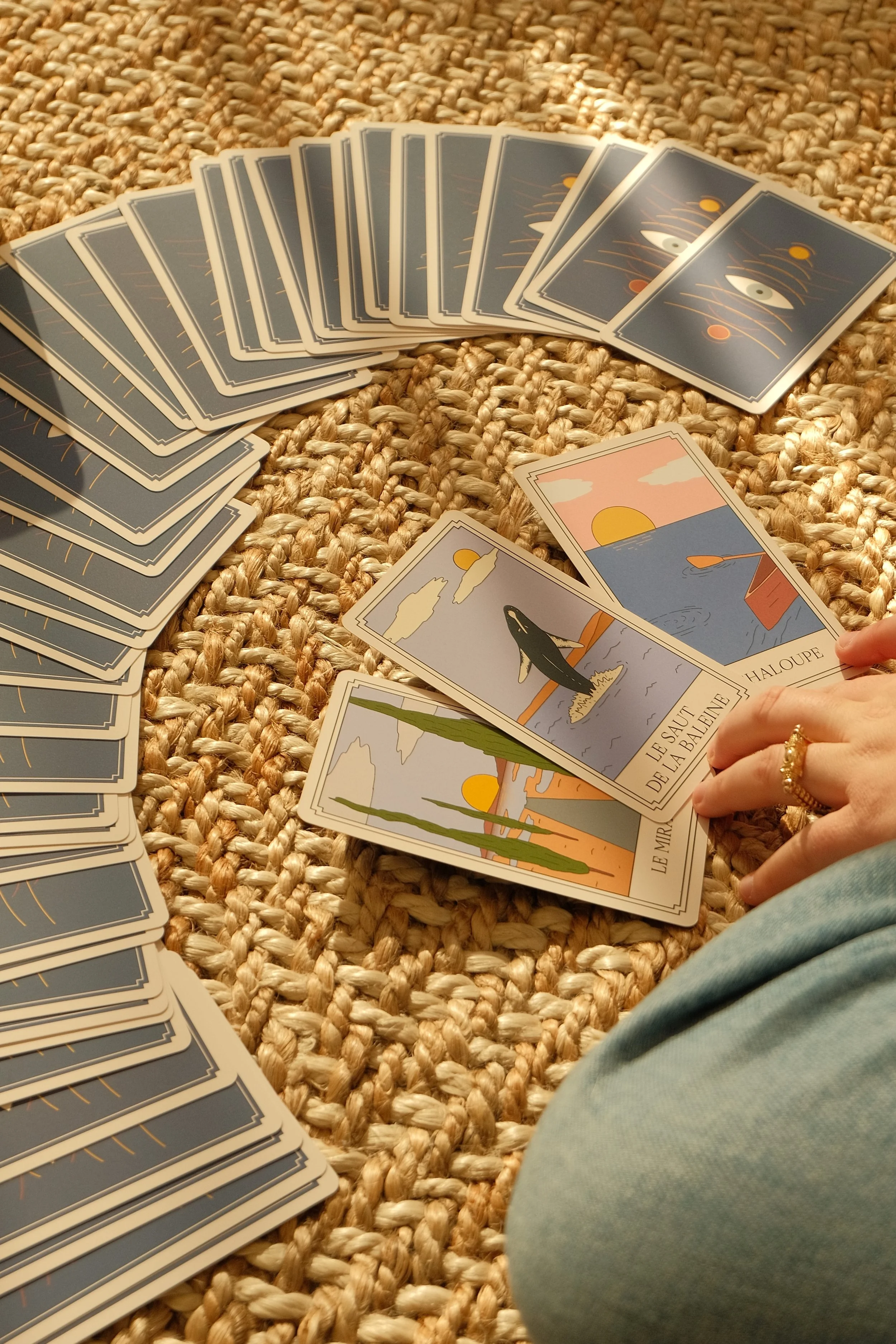 Groupe de cartes de tarot posées sur un tapis en corde, avec quelques cartes visibles à l'avant montrant des illustrations de paysages et de symboles.