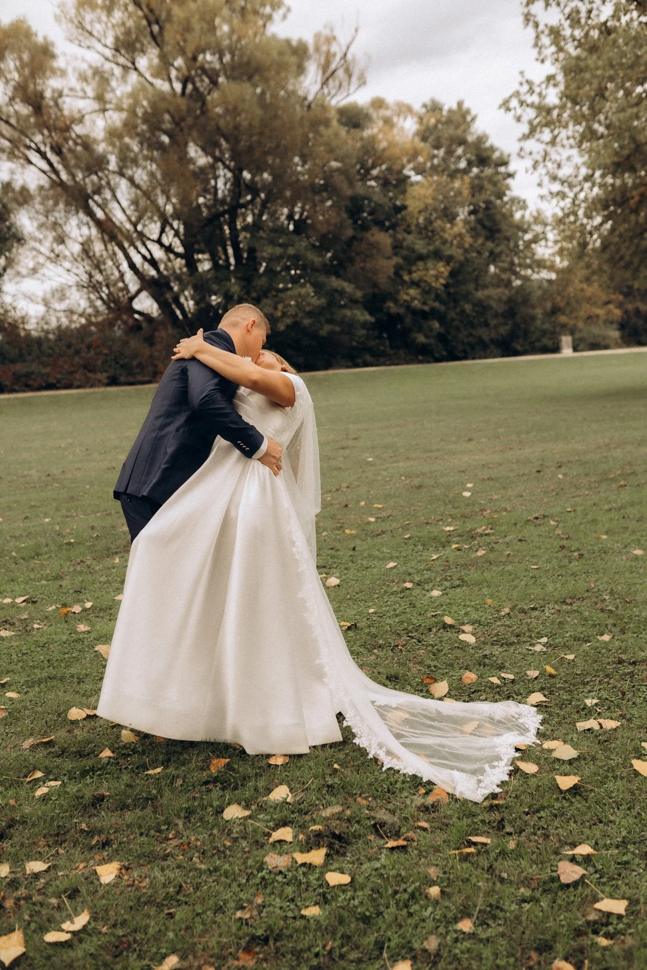Ein glückliches Brautpaar küsst sich innig in einem Park voller Herbstlaub bei einem romantischen Hochzeitsfotoshooting in Klagenfurt, Kärnten.