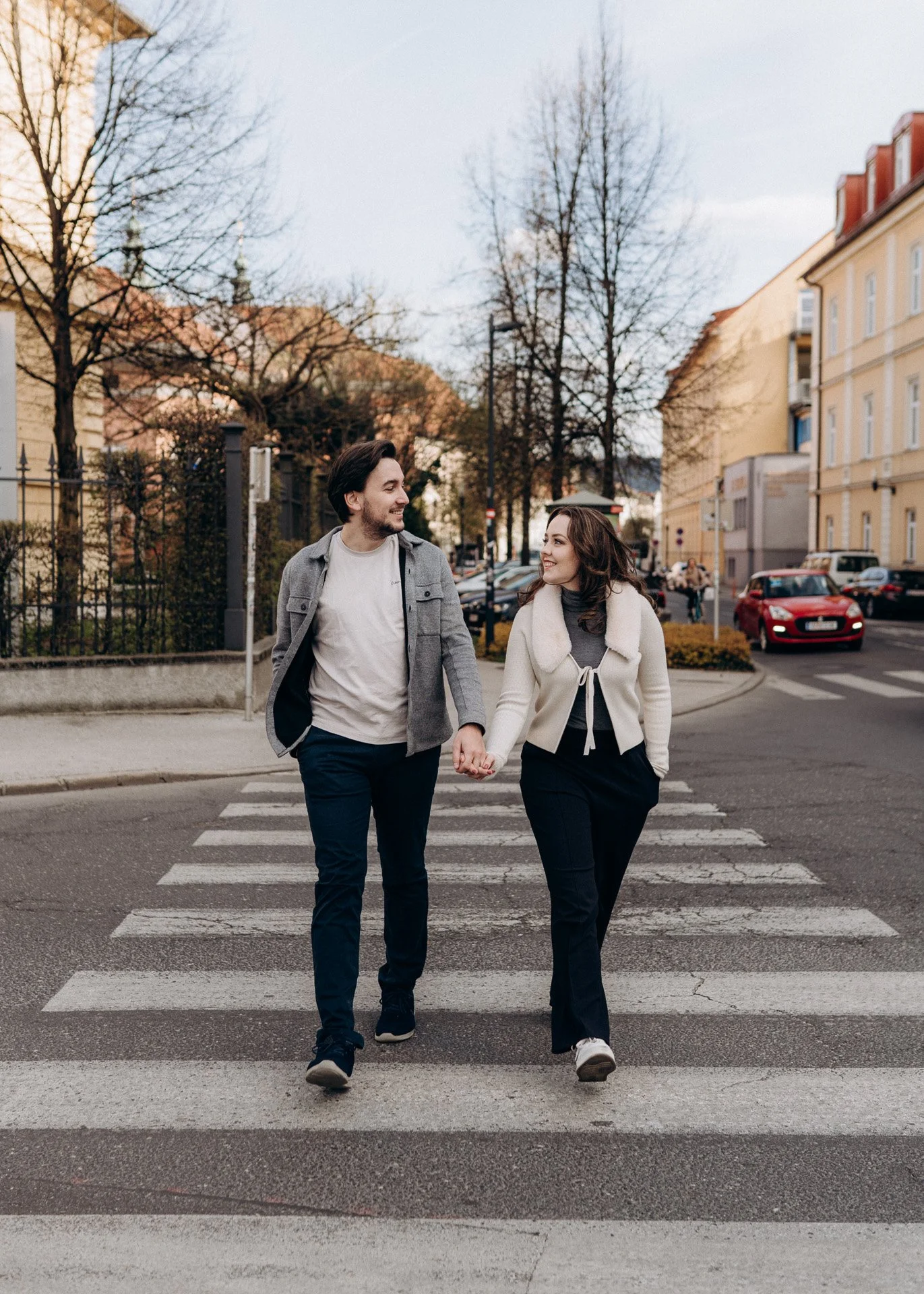 Urbane Romantik: Ein glückliches Paar hält Händchen und lächelt sich bei einem gemütlichen Spaziergang an – festgehalten bei einem Outdoor-Fotoshooting in Kärnten.