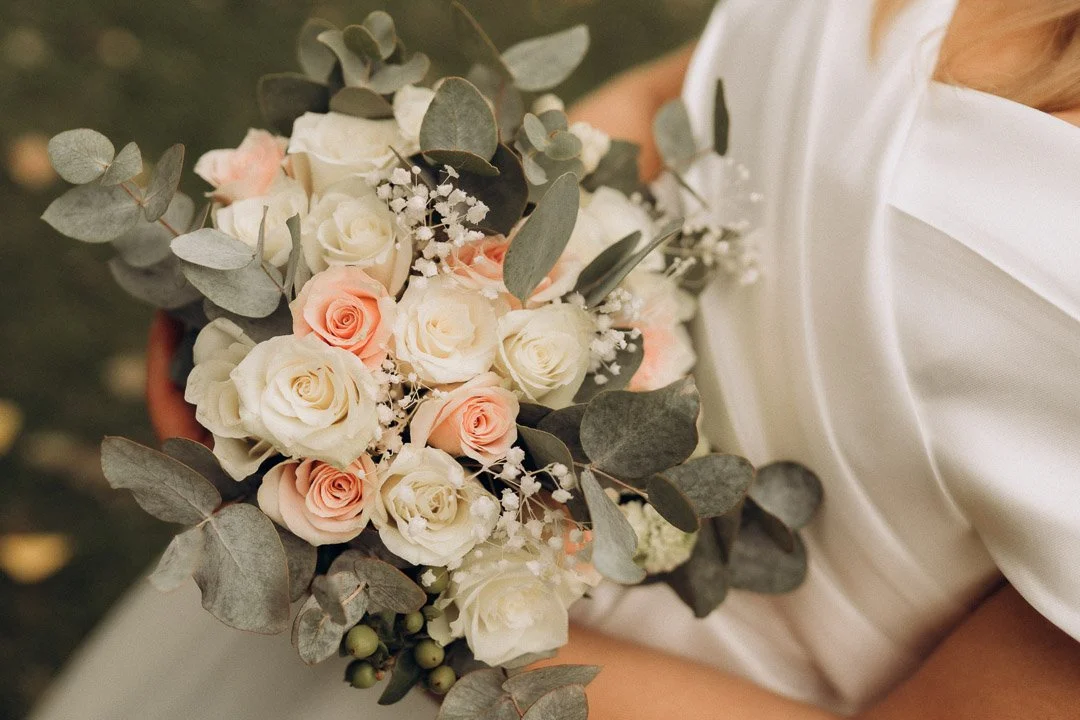 Nahaufnahme eines Brautstraußes mit weißen und pastellrosa Rosen sowie Eukalyptus, gehalten von der Braut bei einer Hochzeit in Kärnten.