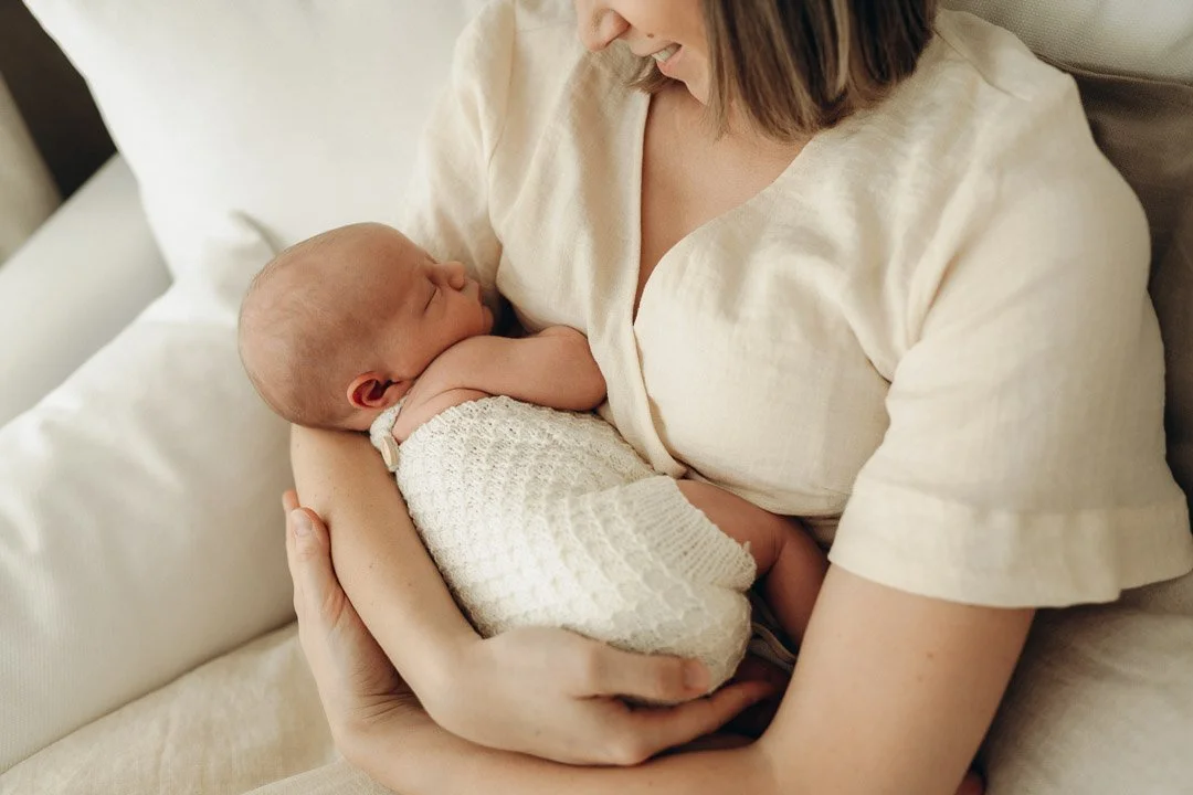 Ein neugeborenes Baby schläft geborgen in den Armen seiner Mutter bei einem Neugeborenen-Fotoshooting in Klagenfurt,Kärnten.