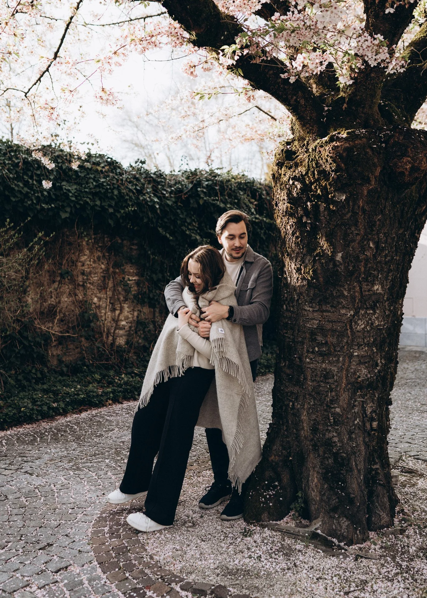 Ein Mann und eine Frau umarmen sich unter einem blühenden Baum während eines romantischen Love Story Shootings in Klagenfurt.