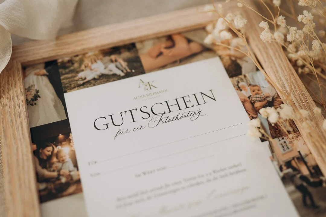 Geschenkgutschein für ein Fotoshooting, umgeben von Familienfotos in einem Holzrahmen, mit Blumen dekoriert.