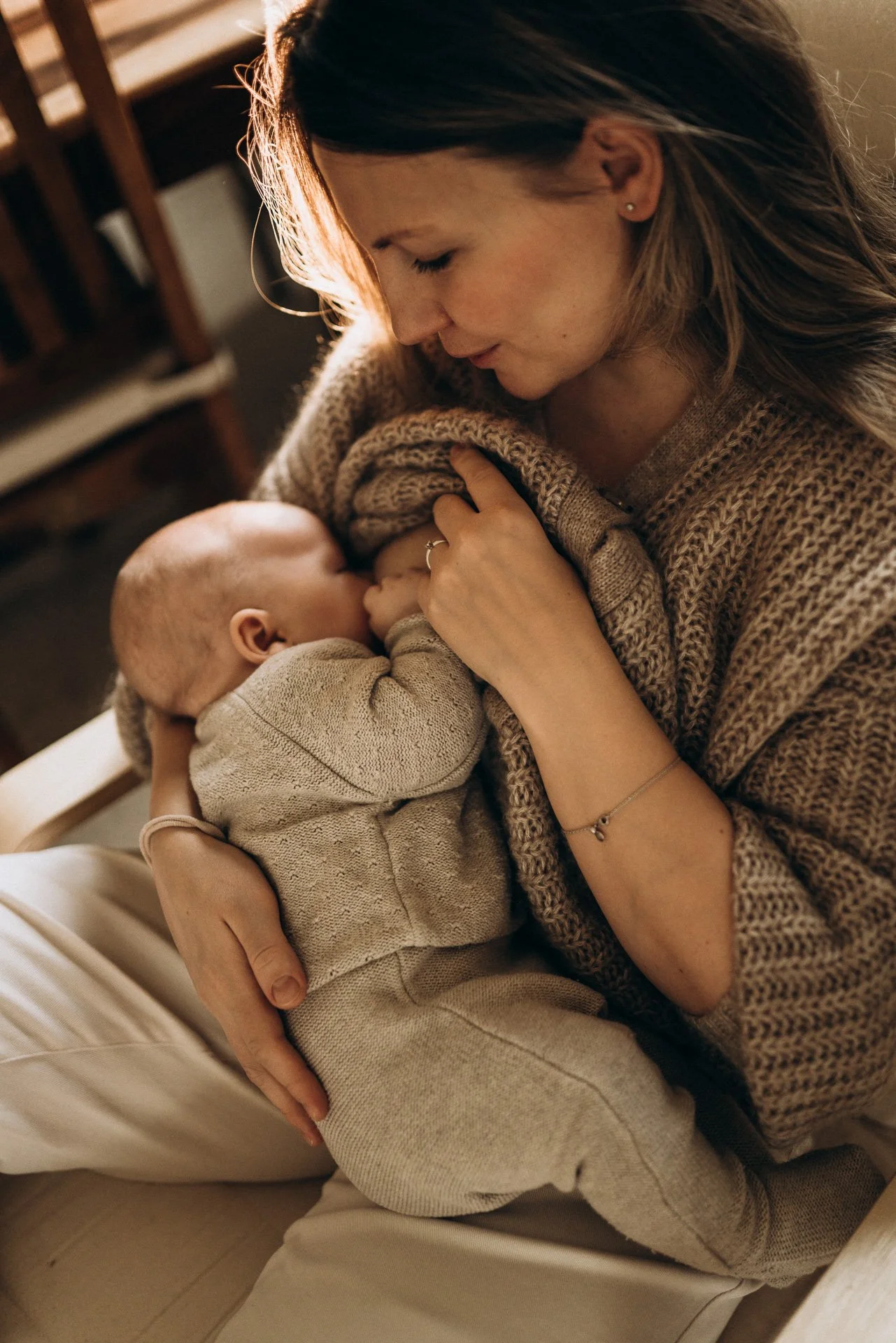 Frau hält ein Baby im Arm und stillt es, während sie auf einem Stuhl sitzt.