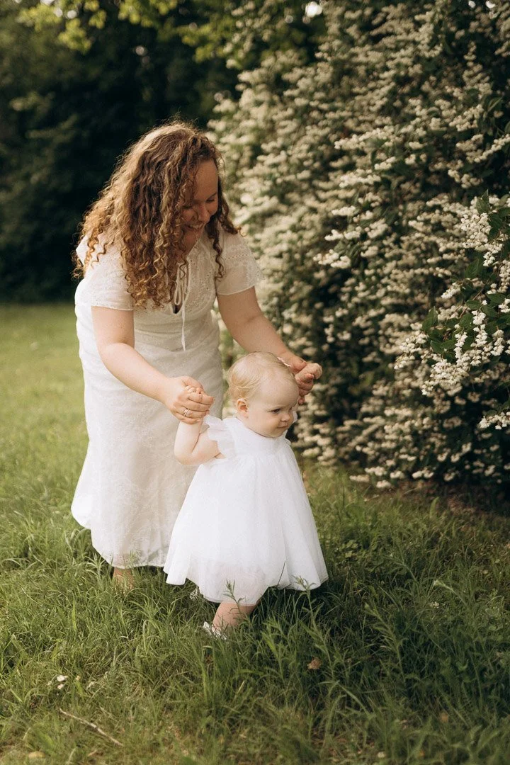 Eine Mutter und ihre kleine Tochter gehen Hand in Hand über eine grüne Wiese beim Familienfotoshooting in Klagenfurt, Kärnten.