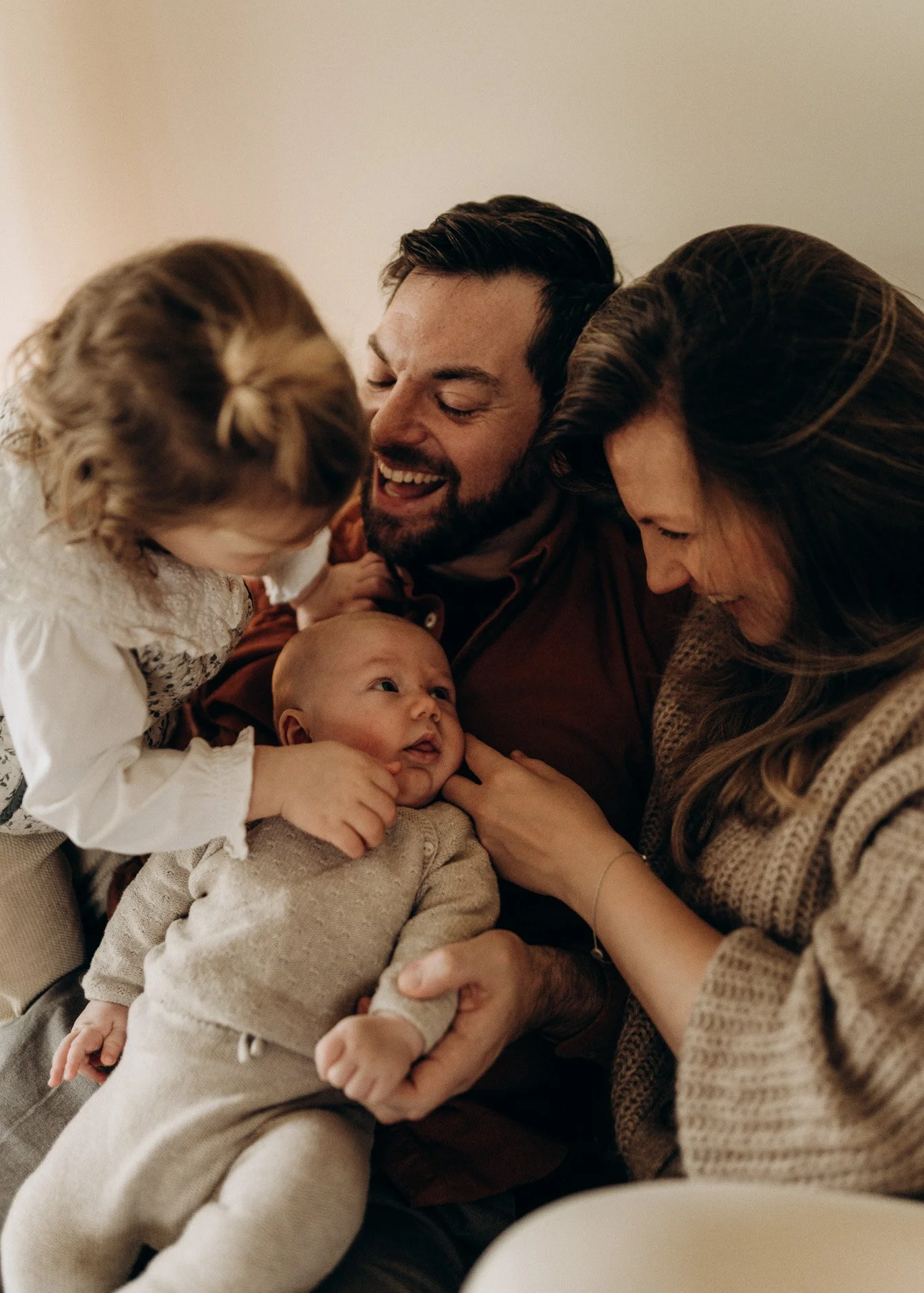 Eine glückliche Familie besteht aus einem Mann, einer Frau, einem kleinen Mädchen und einem Baby, die eng um das Baby herum sitzen und lachen.