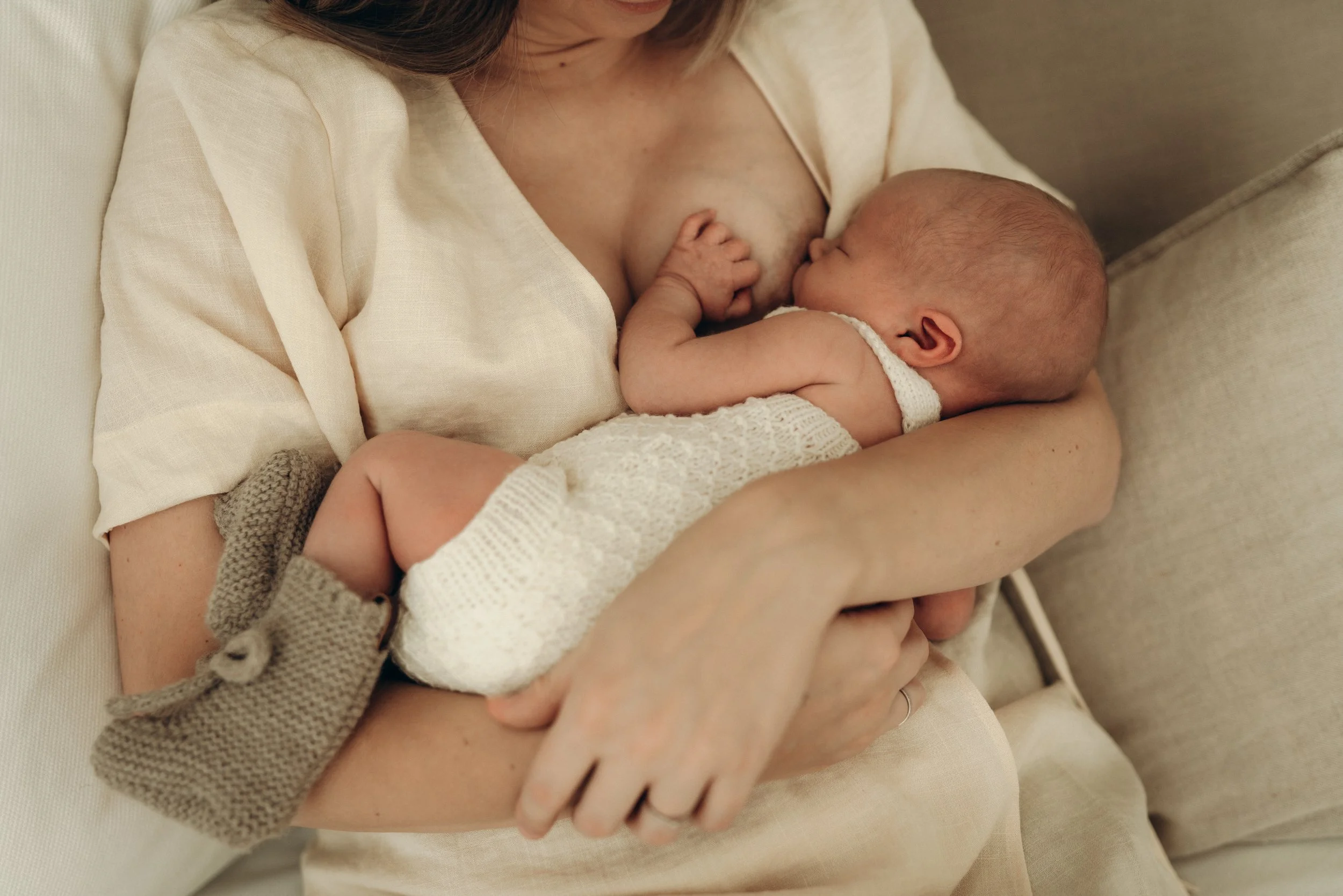 Eine Mutter stillt ihr neugeborenes Baby an ihrer Brust, während sie auf einem Sofa sitzt.