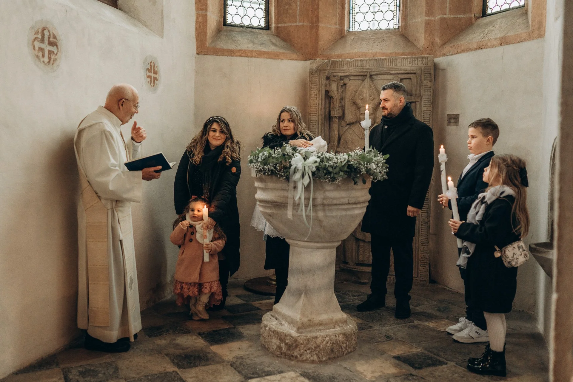 Eine Gruppe von Menschen bei einer religiösen Zeremonie in einer Kirche, mit Kerzen und einem Taufbecken.