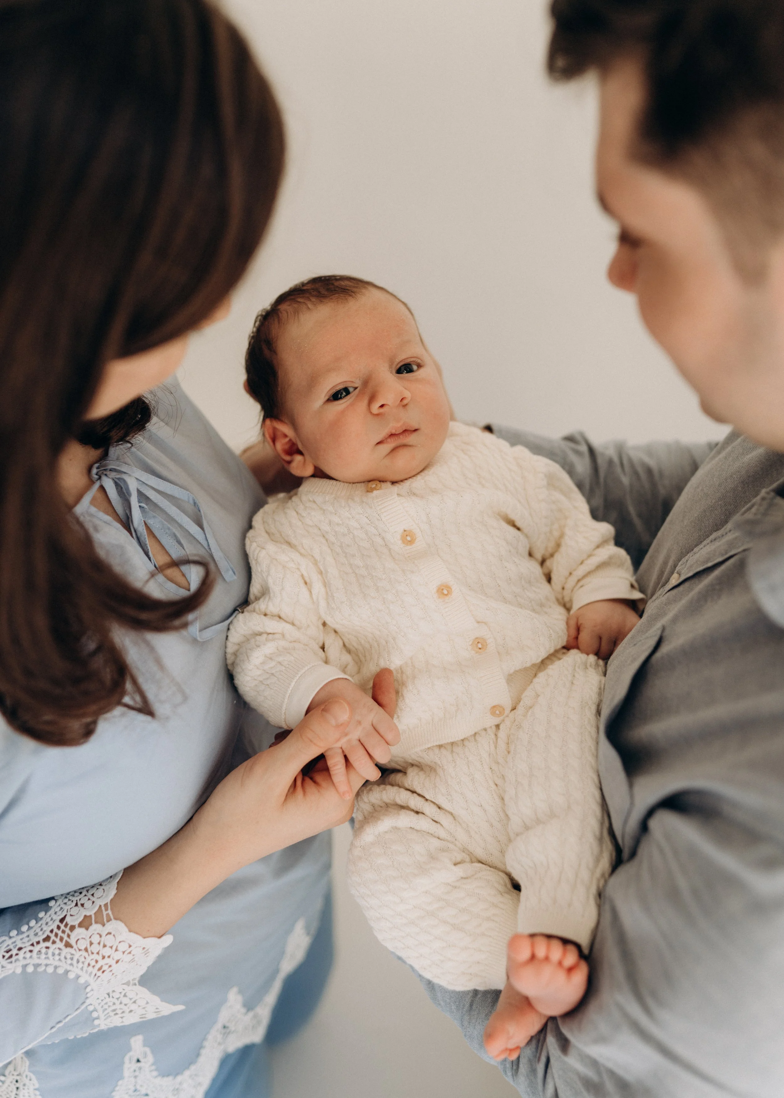 Ein Baby gehalten von seinen Eltern, die sich gegenseitig anschauen während eines Neugeborenen-Fotoshootings in Klagenfurt, Kärnten.