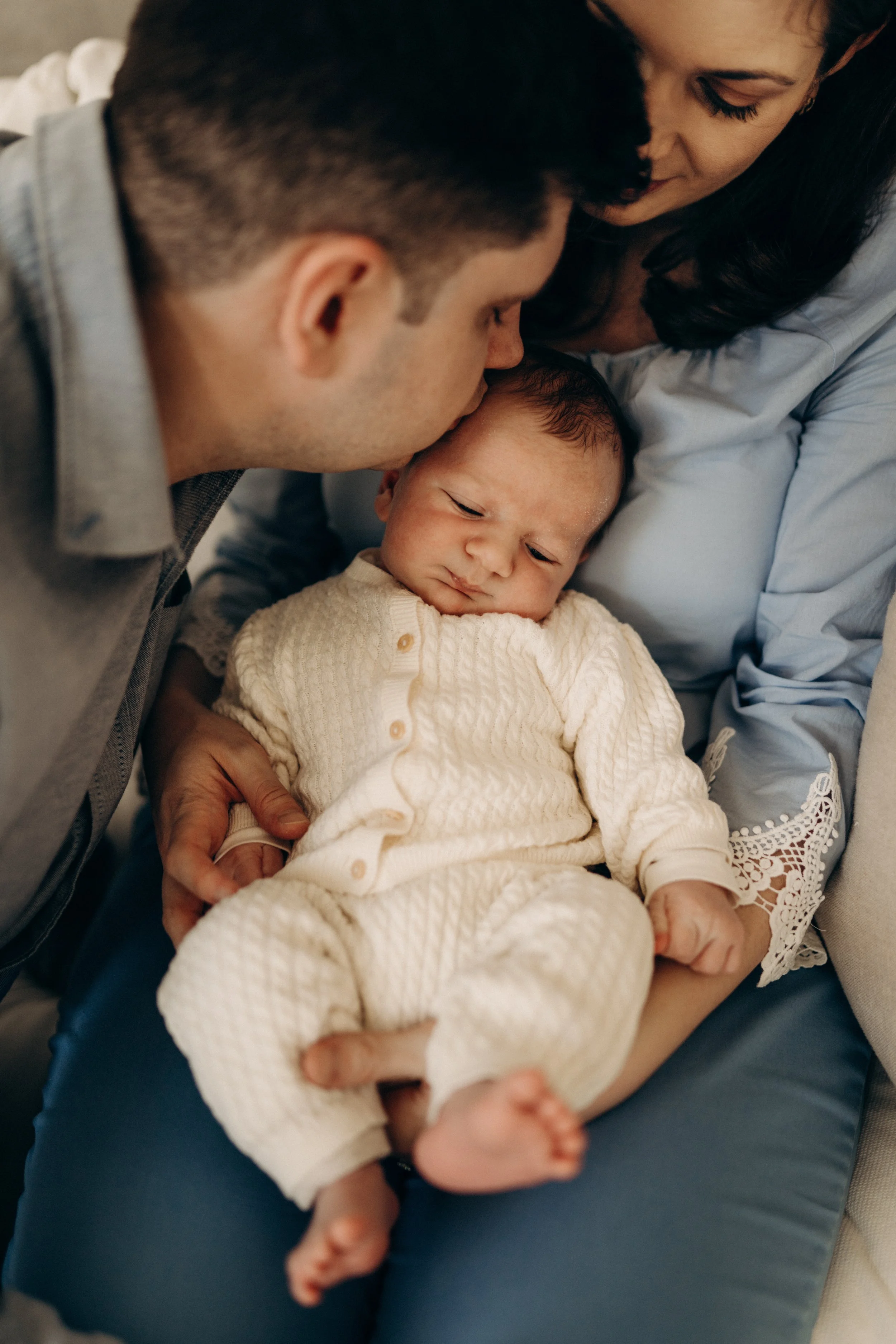 Ein Baby wird von einem Mann und einer Frau gehalten, die sich liebevoll um das Baby kümmern, während es auf deren Schoß sitzt.