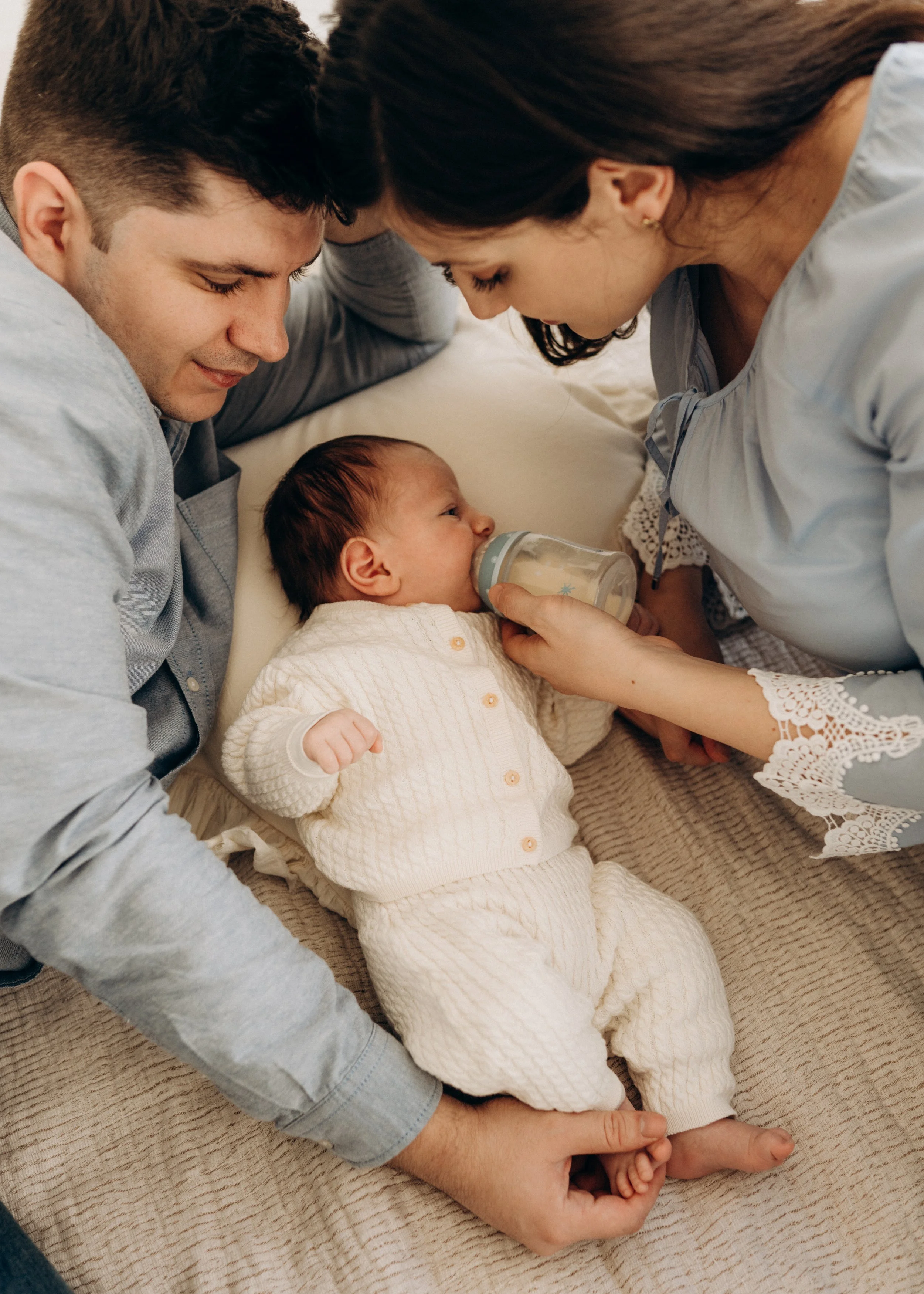 Liebevolle Eltern sehen ihrem Baby beim Trinken aus der Flasche zu – ein intimer Moment während eines Newborn-Fotoshootings in Klagenfurt.