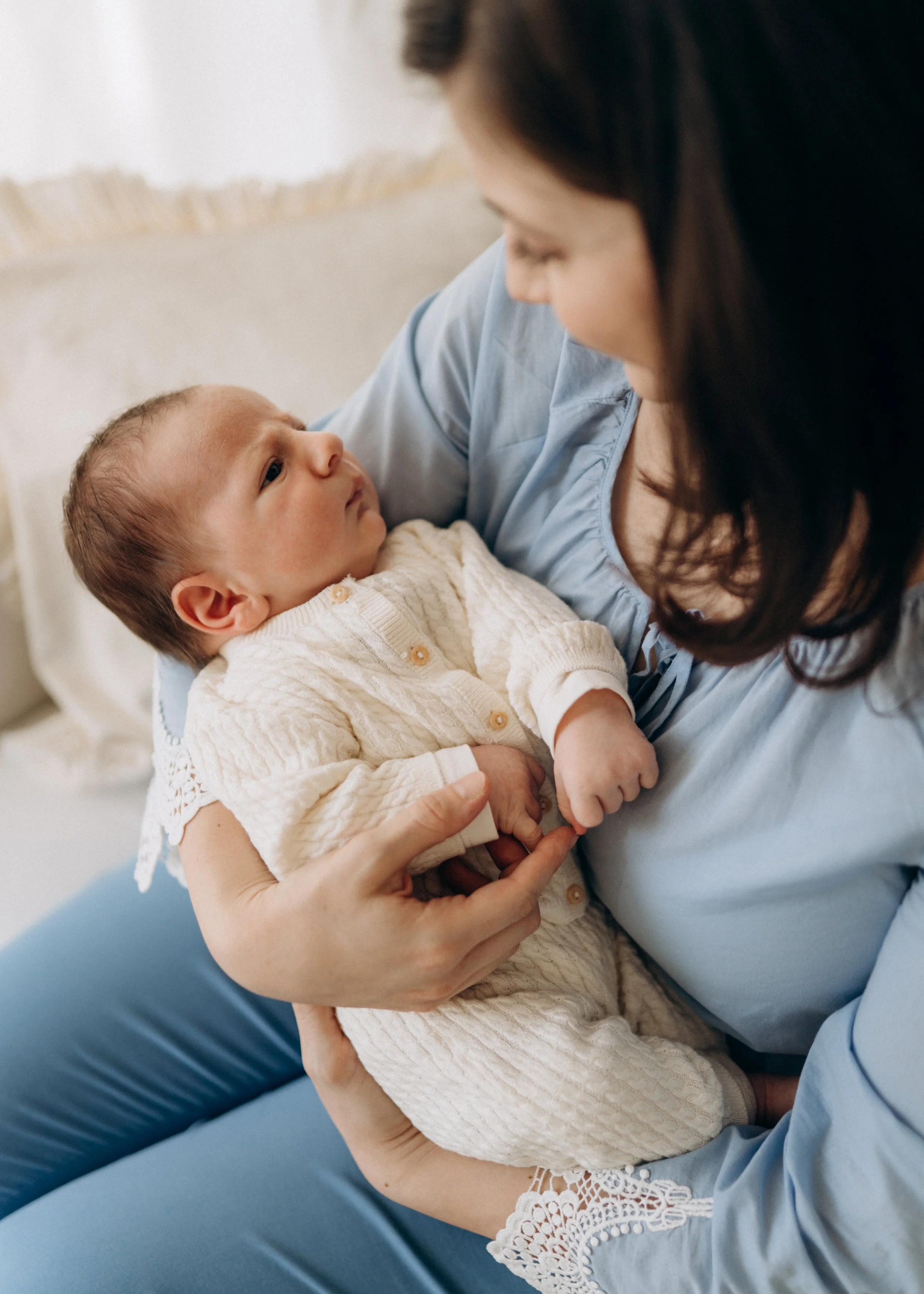Eine Frau hält ein Baby in den Armen und schaut liebevoll auf das Kind, das sie auf ihrem Schoß sitzen hat, während sie im Krankenhausbett sitzt.