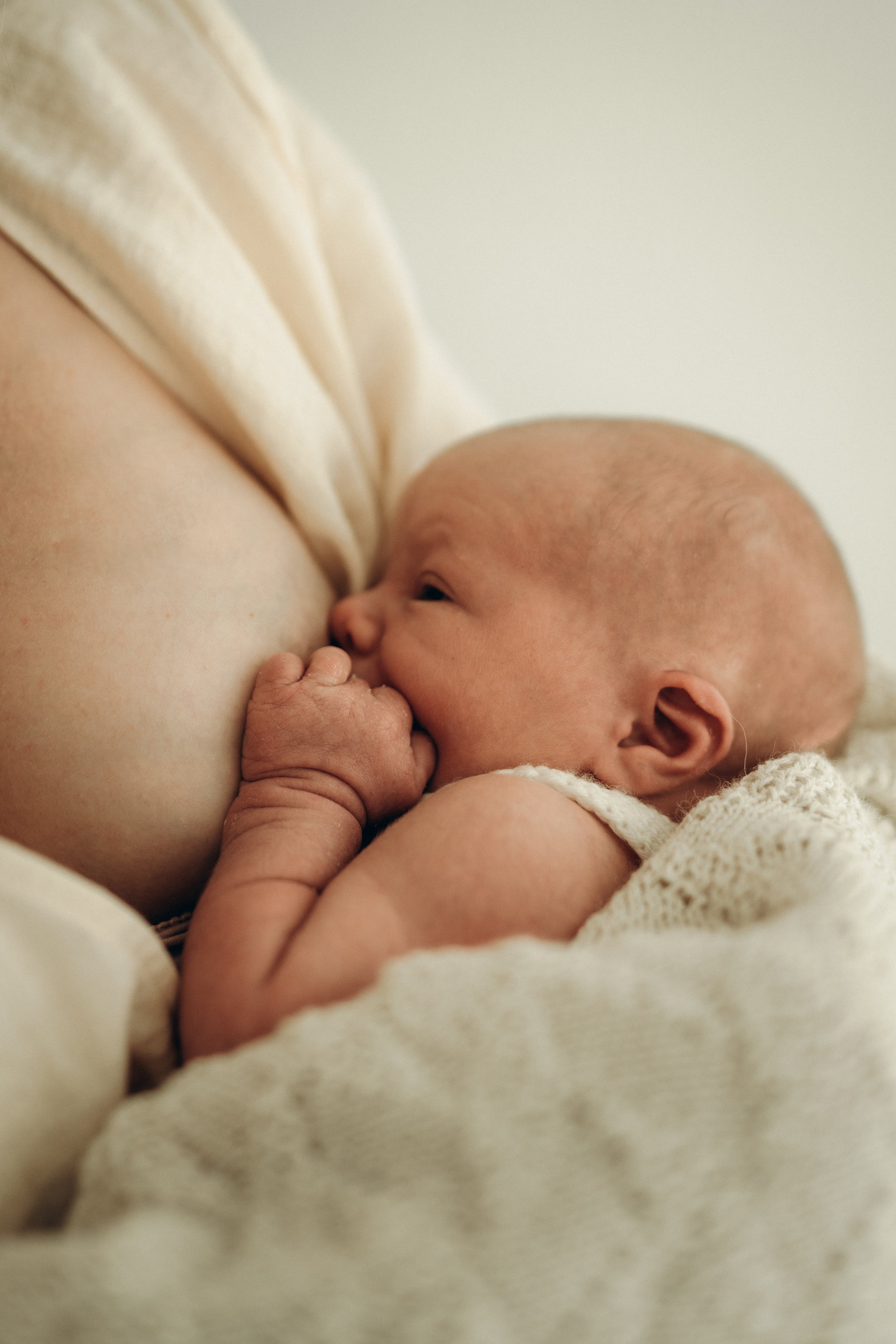 Ein neugeborenes Baby saugt an der Brust seiner Mutter während eines Newborn Fotoshootings in Klagenfurt, Kärnten.