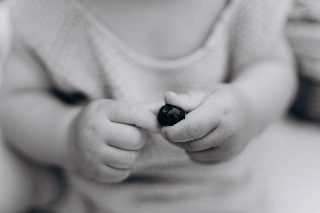 Nahaufnahme von Kinderhänden, die eine dunkle Frucht halten, in Schwarz-Weiß