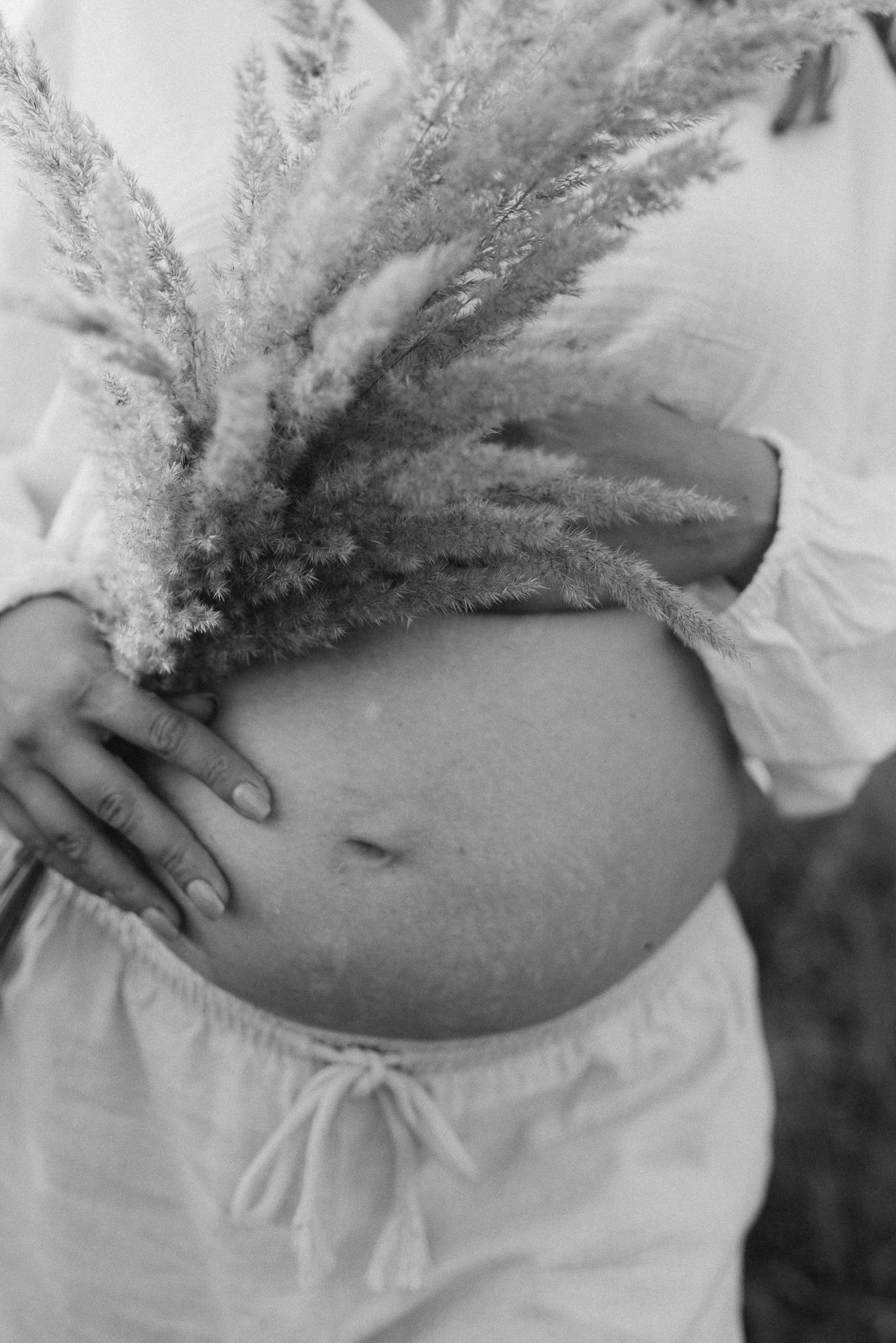 Nahaufnahme eines Bauchnabels mit Hand, die ihn berührt, und einem Kleidungsstück, das um die Taille gebunden ist, in Schwarz-Weiß.