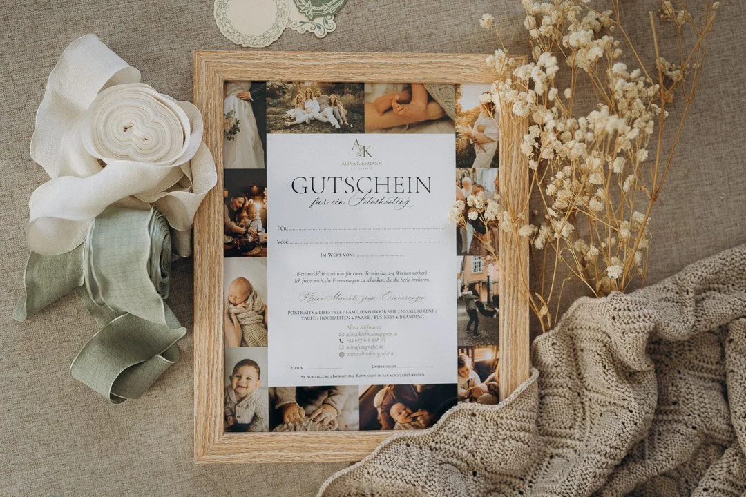 Gutschein für eine Taufe, umgeben von Fotos, Blumenbändern und einer gestickten Decke.