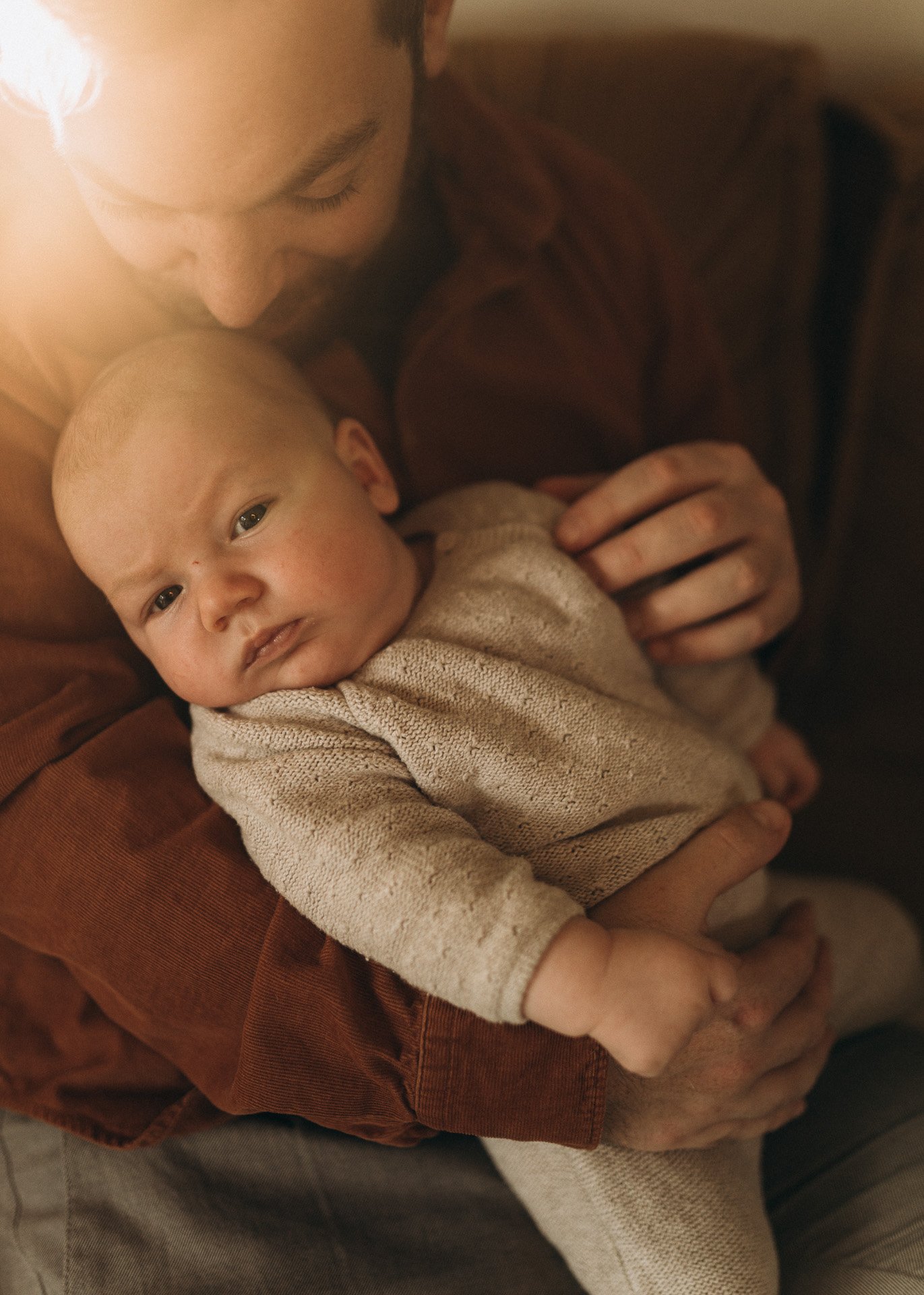 Ein Erwachsener hält ein Baby im Arm. Das Baby schaut direkt in die Kamera, mit einem neutralen Ausdruck.