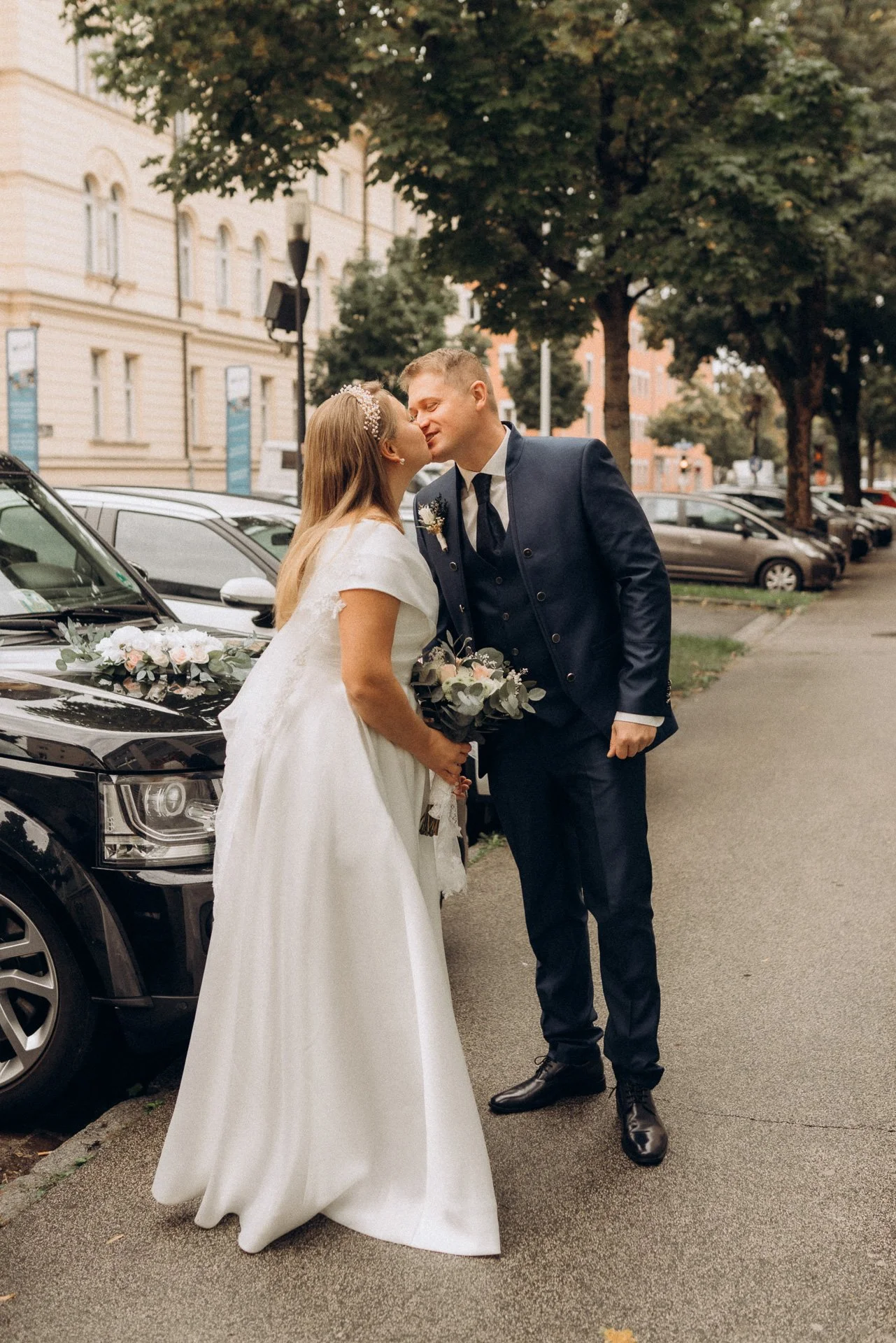 Romantischer Moment: Ein Brautpaar küsst sich vor dem dekorierten Hochzeitsauto während des Hochzeitsfotoshootings in Klagenfurt.