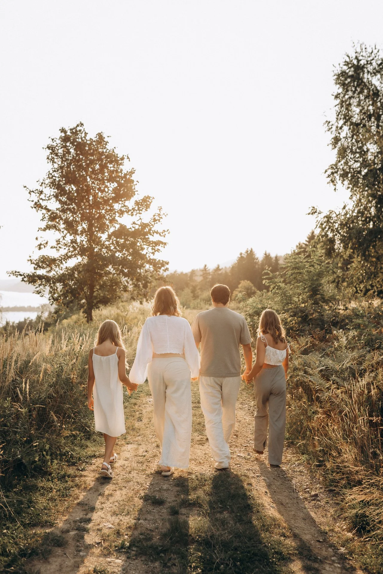 Eine Familie läuft gemeinsam auf einem unbefestigten Weg durch die Natur, umgeben von Bäumen und Gras, bei Sonnenuntergang.