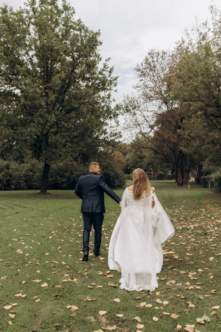 Ein Brautpaar läuft im Herbst gemeinsam über eine Parkwiese, fotografiert beim Wedding Photoshoot in Klagenfurt, Kärnten.