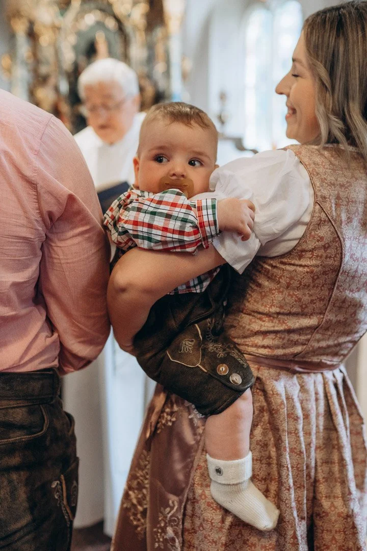 Ein Baby in traditioneller Kleidung, gehalten von seiner Mutter während einer feierlichen Taufreportage in Kärnten.