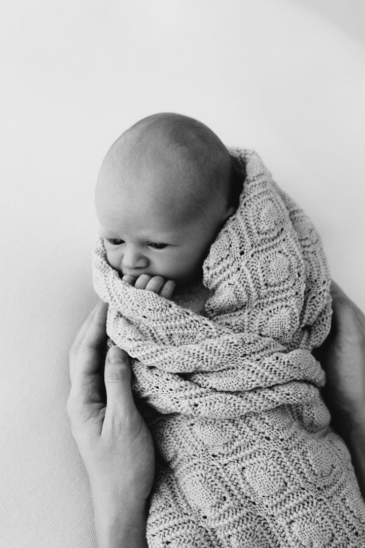 Ein Baby, das in ein gestricktes Tuch gehüllt ist, wird liebevoll gehalten während eines Newborn-Fotoshootings in Klagenfurt, Kärnten.