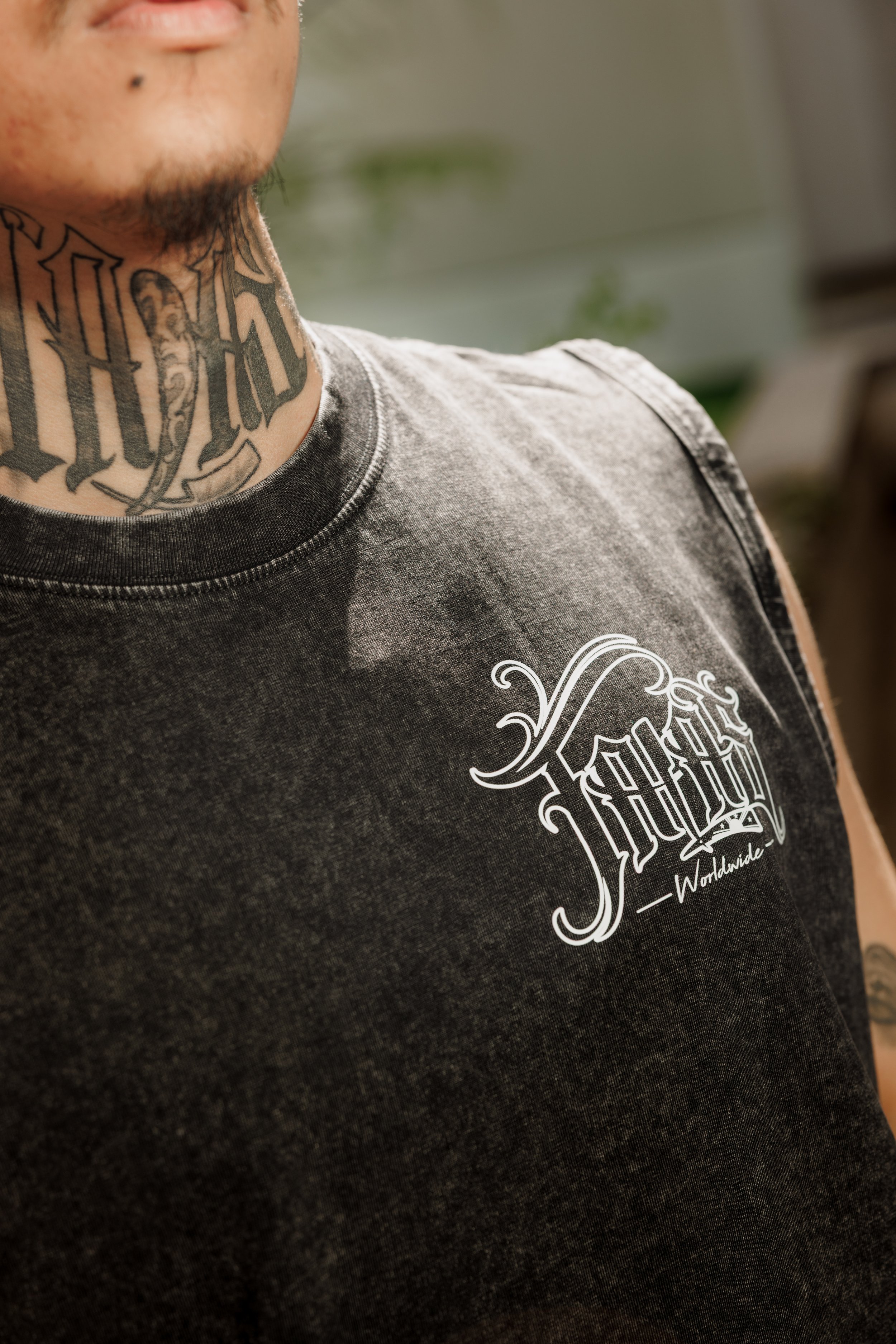 A person with a neck tattoo wearing a sleeveless black t-shirt with white graphic design.