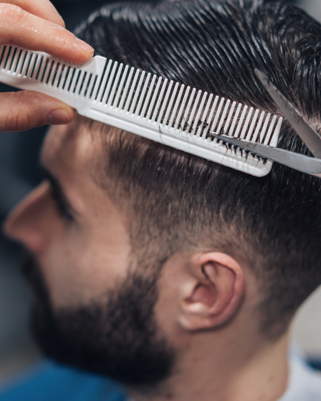 A barber trims a man's dark, wet hair with scissors and a fine-tooth comb.