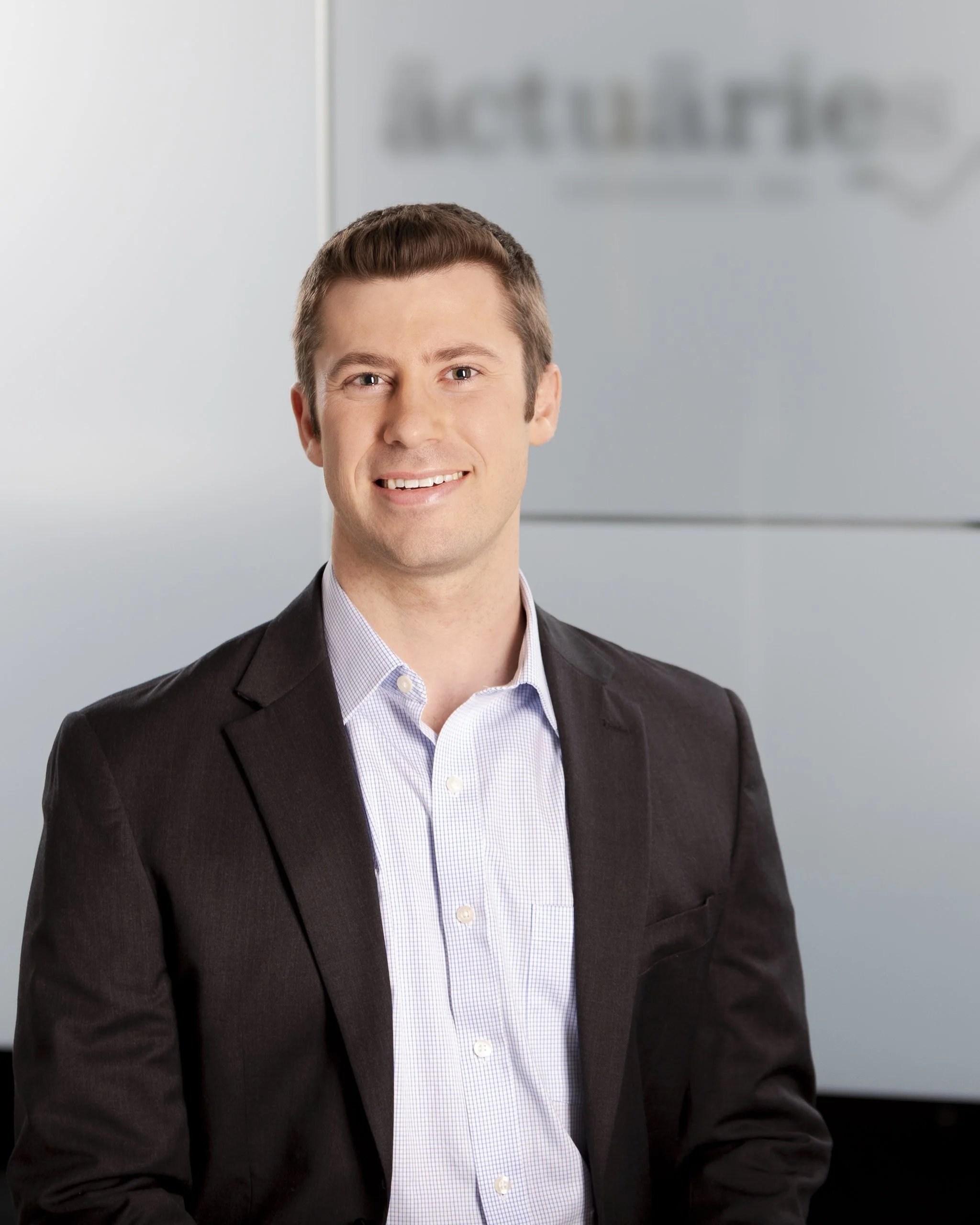 A professional man in a business suit smiling in front of a blurred background with the Accenture logo.