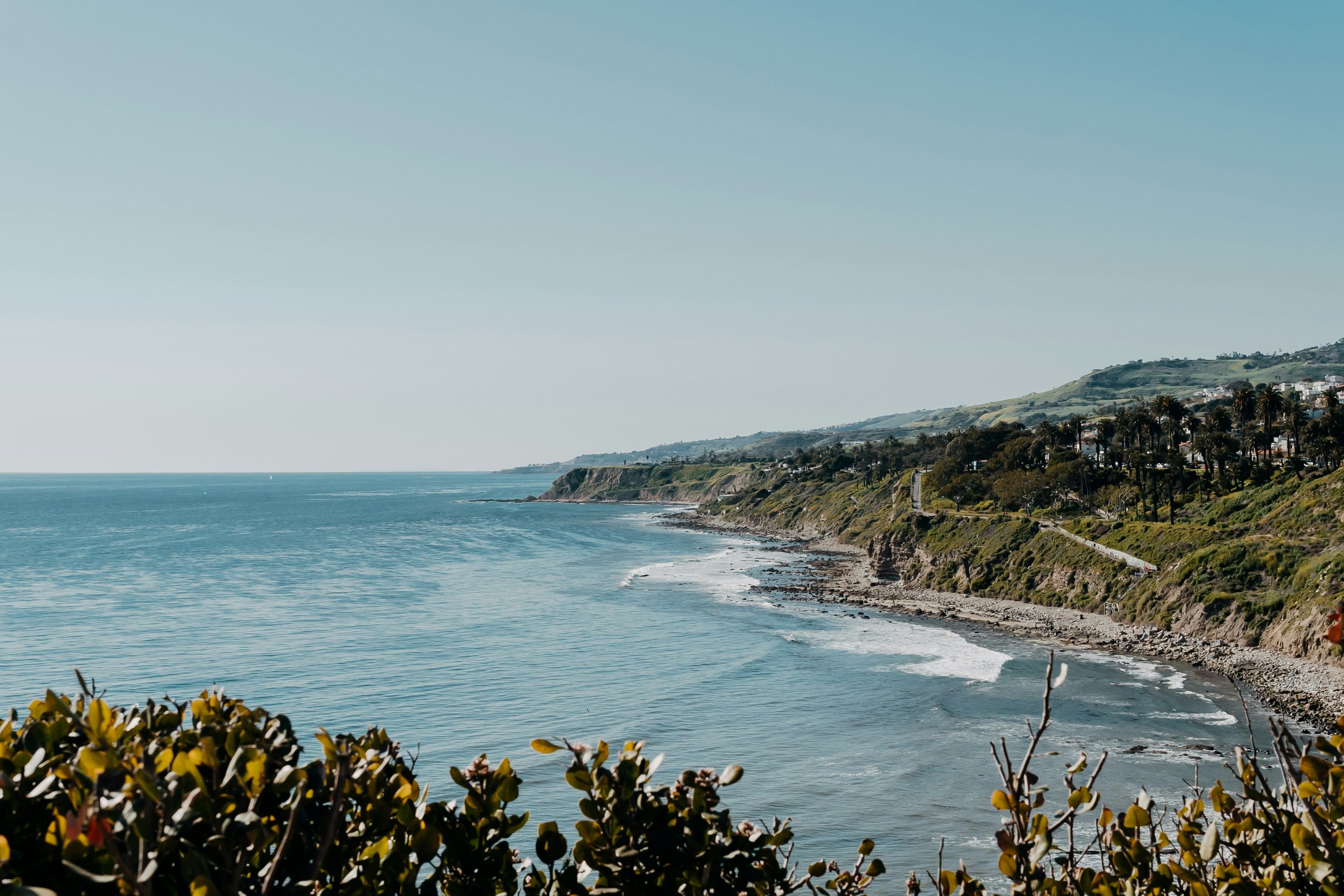 Coastal view with the ocean, cliffs, and houses along the hillside with clear blue sky.